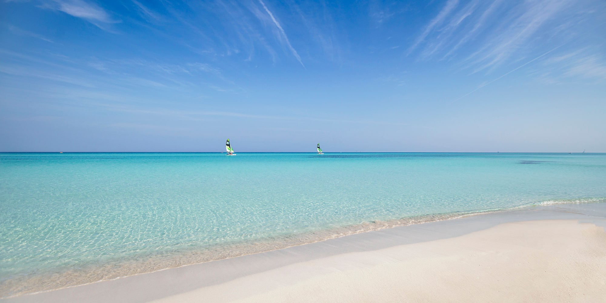 a beach with a couple of windsurfers in the water