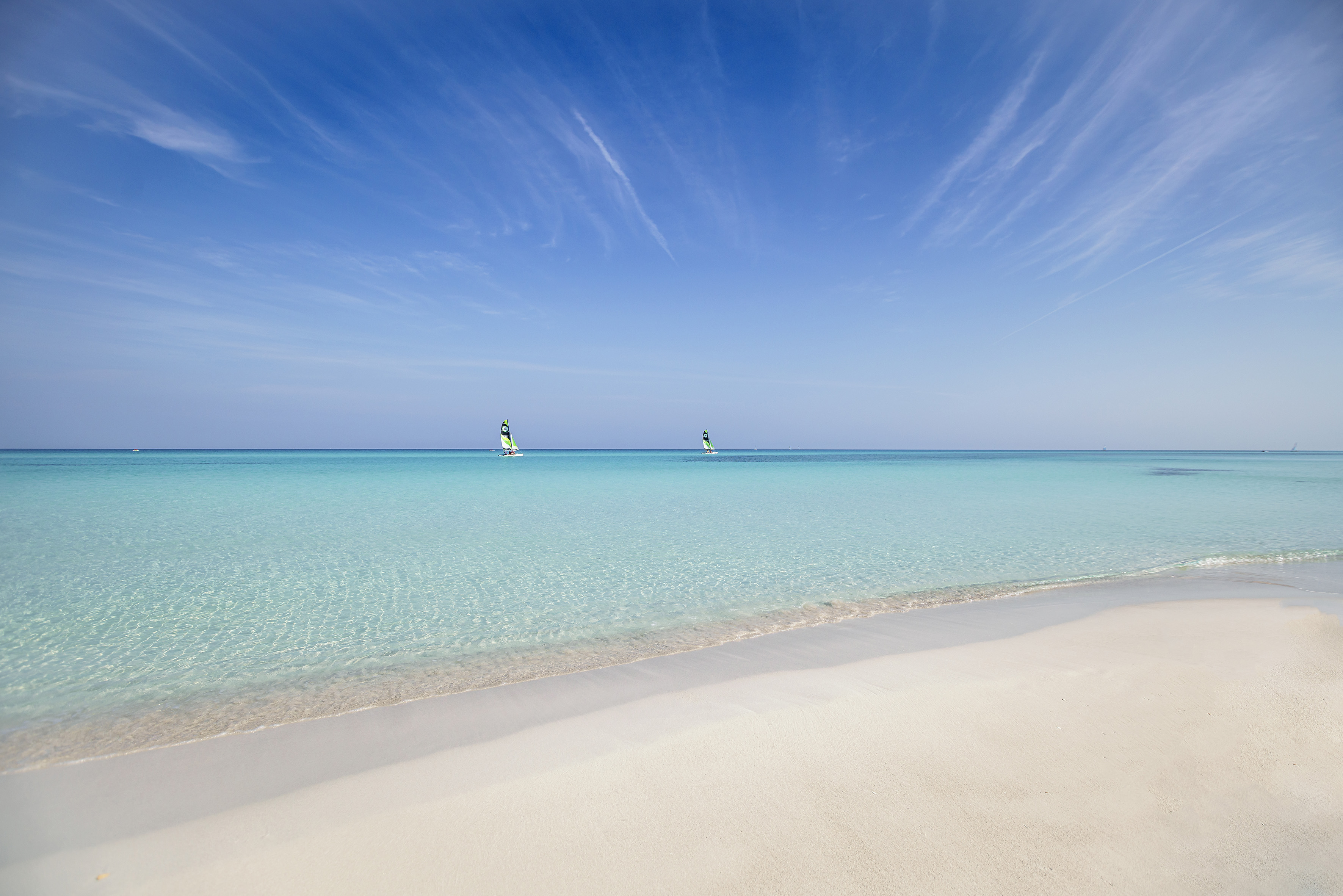 a beach with a couple of windsurfers in the water