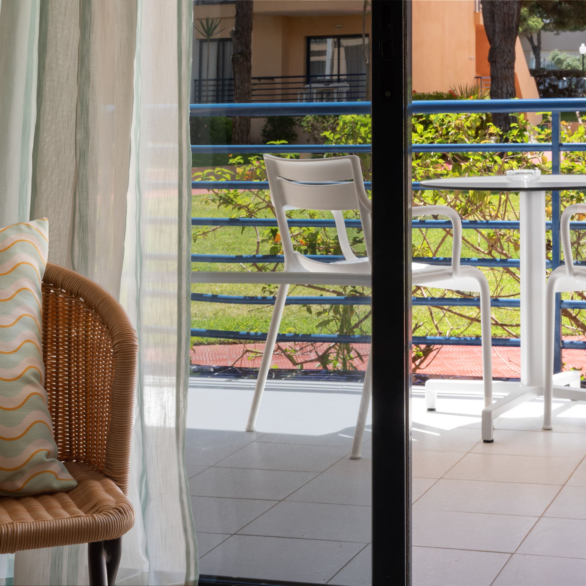 Hotel room balcony with outdoor table, chairs, and garden view.