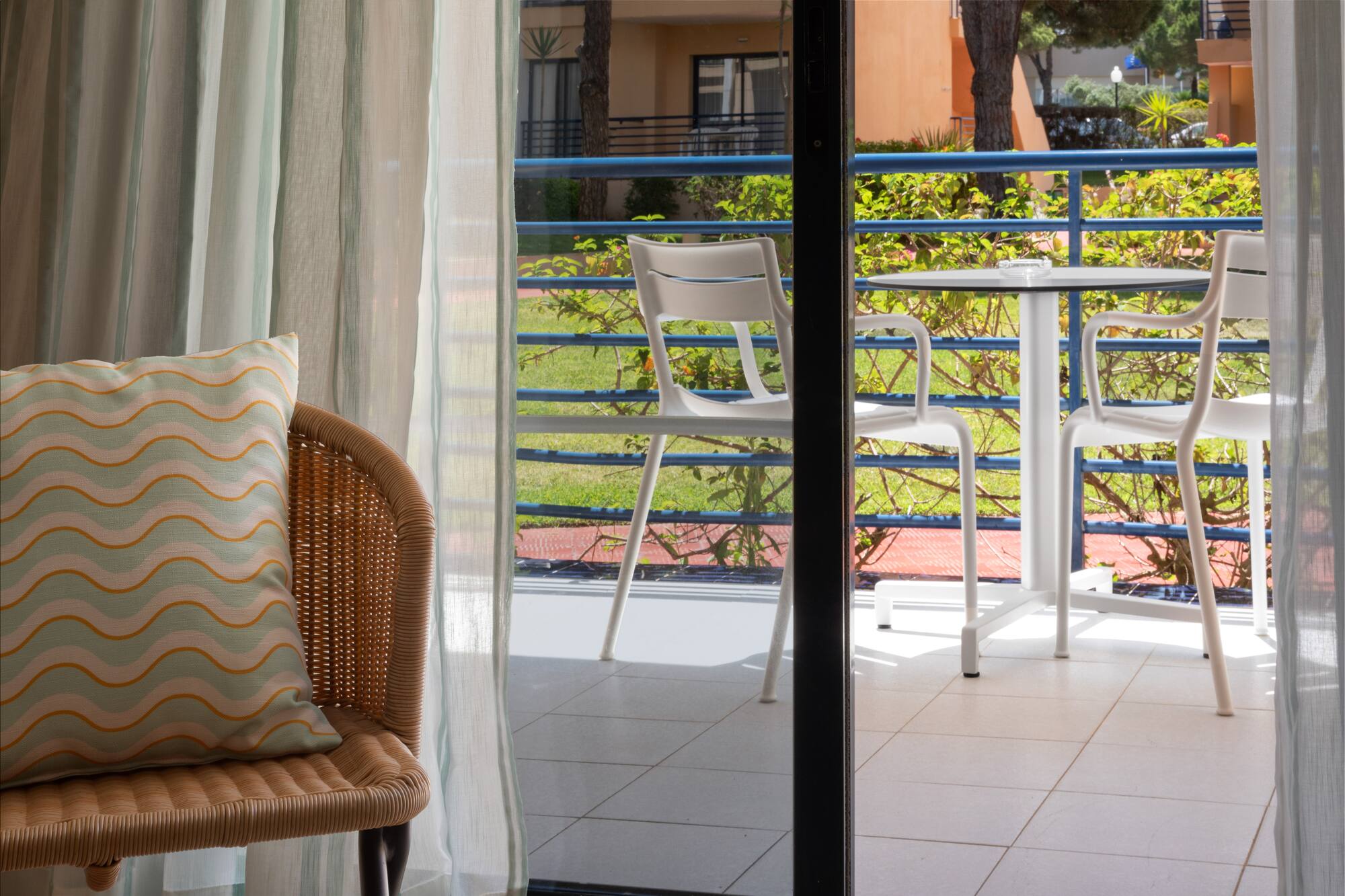Hotel room balcony with outdoor table, chairs, and garden view.