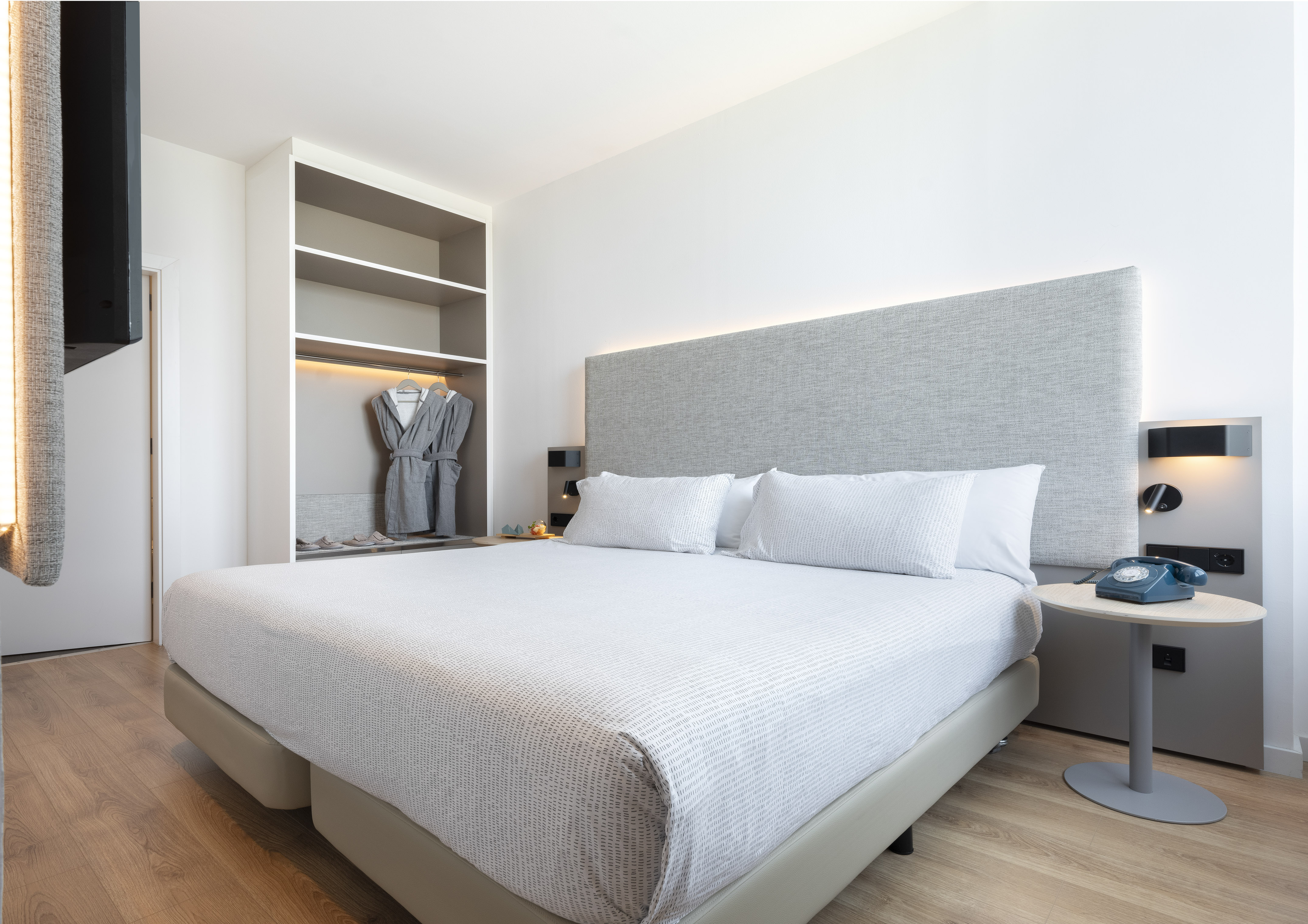 Bright modern hotel room with queen bed, gray headboard, built-in closet with robes.