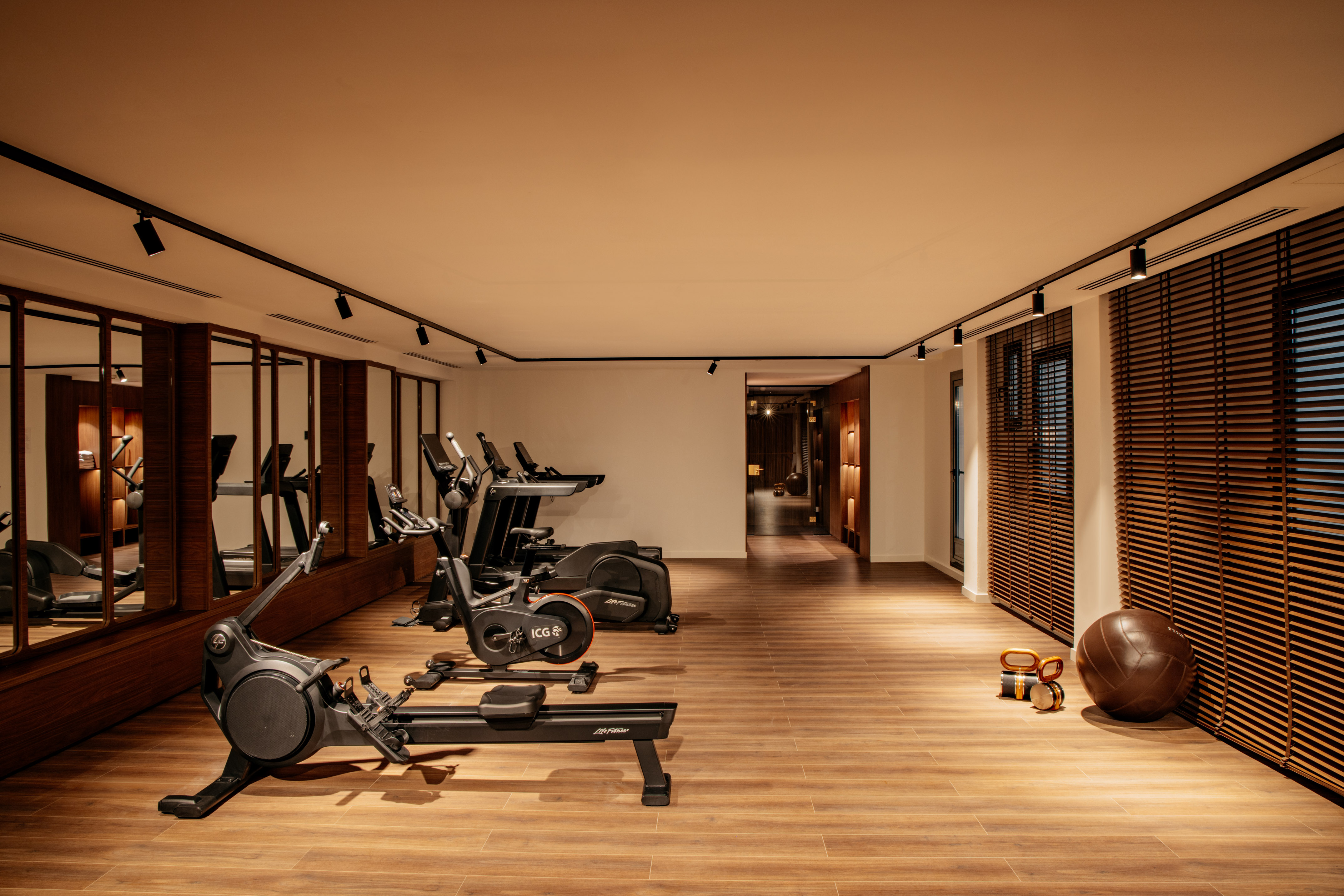 Spacious gym with modern exercise equipment, wood floor, and mirrored wall.
