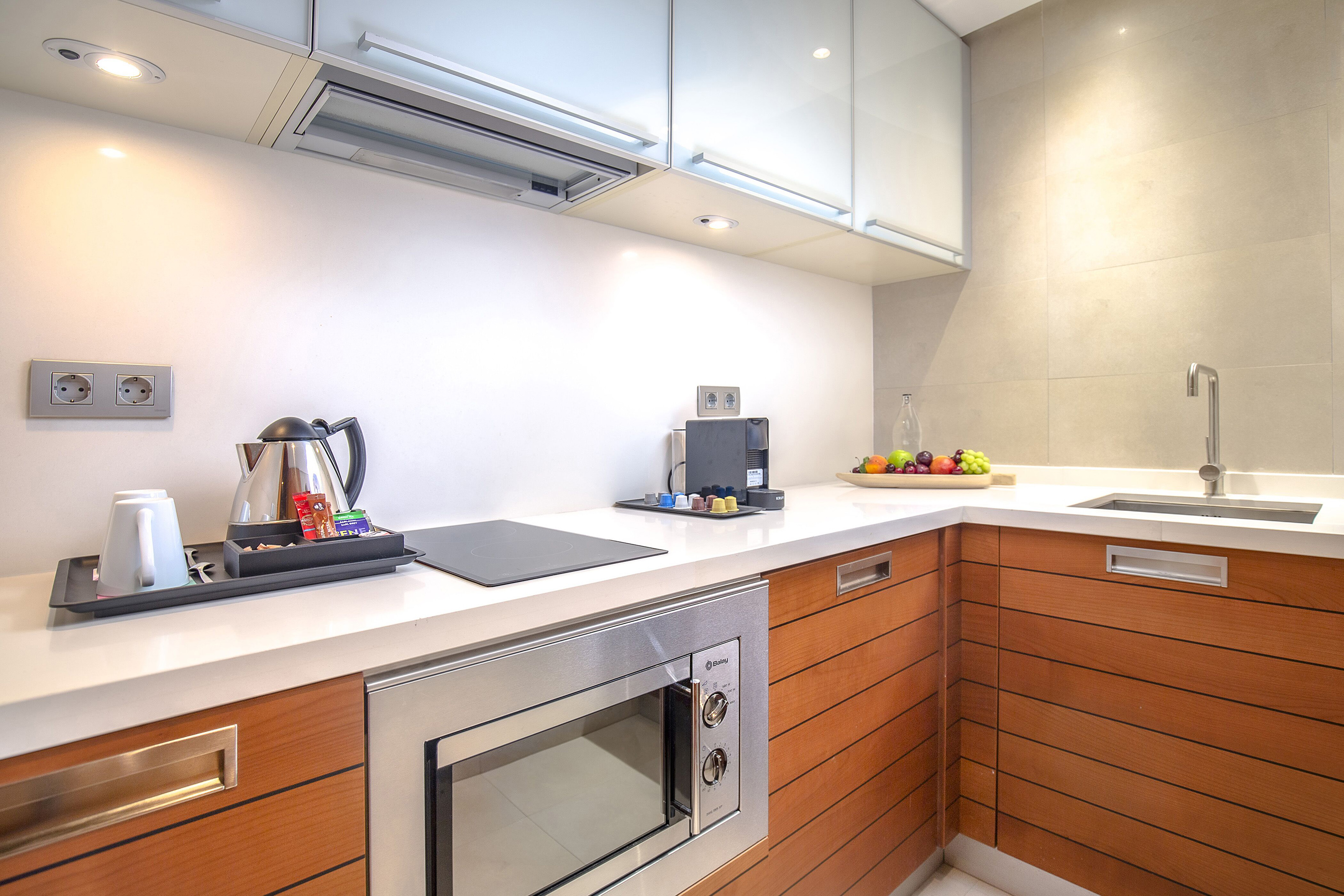 Modern kitchenette with wood cabinets, microwave, cooktop, and coffee station.