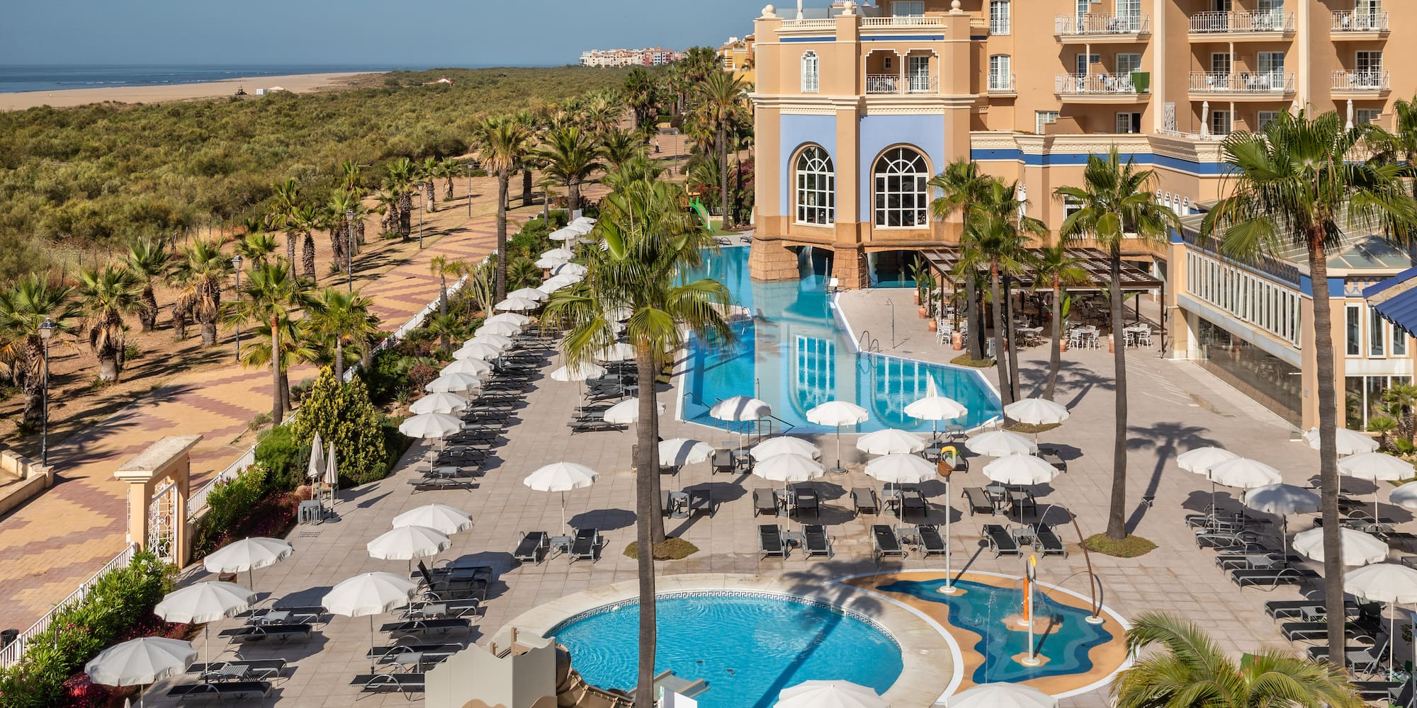 Hotel resort complex with multiple pools, palm trees, and beach.