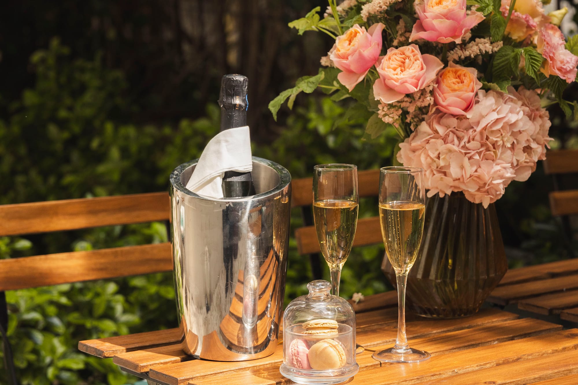 Outdoor patio table with champagne, macarons, and a pink rose bouquet.