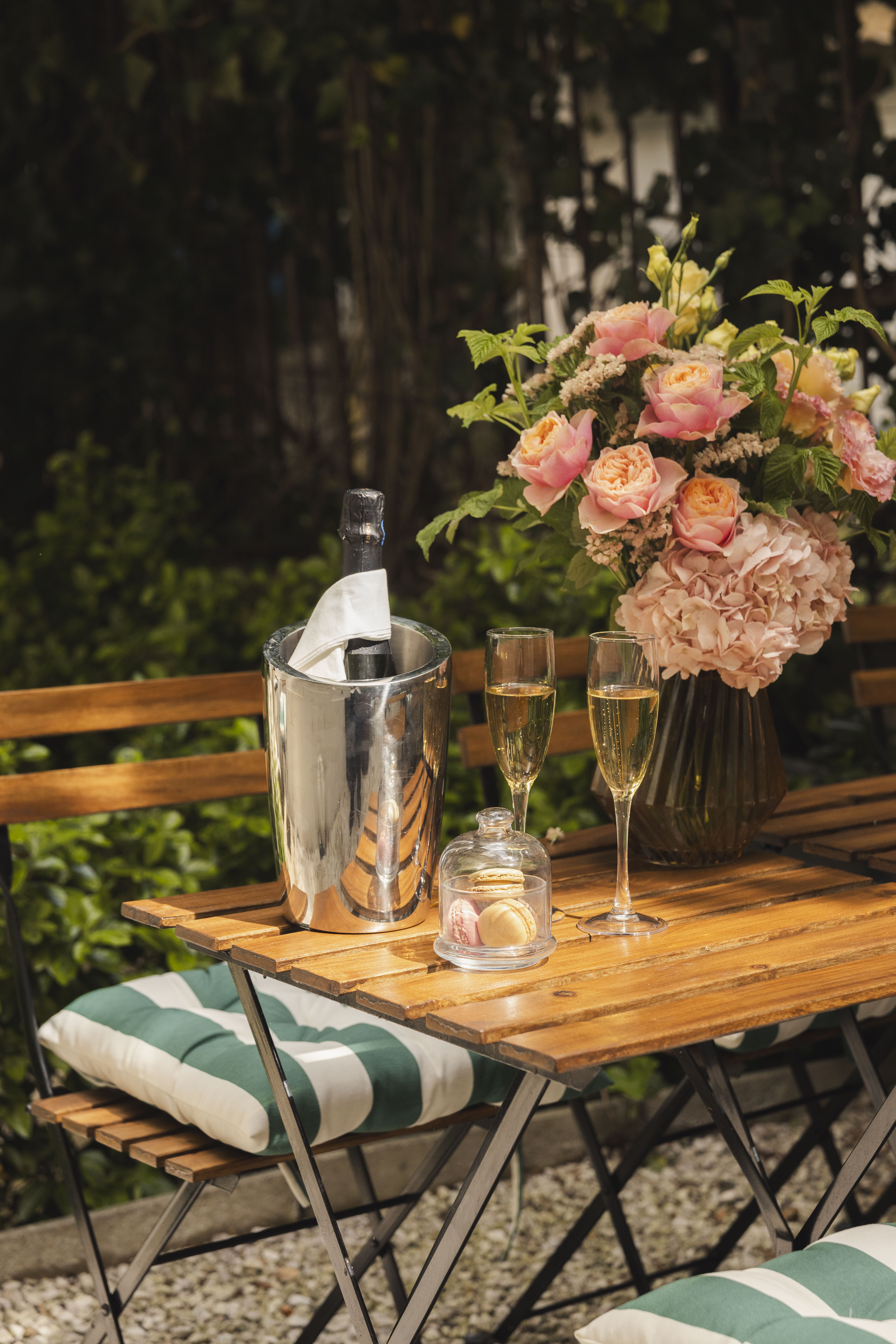 Outdoor patio table with champagne, macarons, and a pink rose bouquet.
