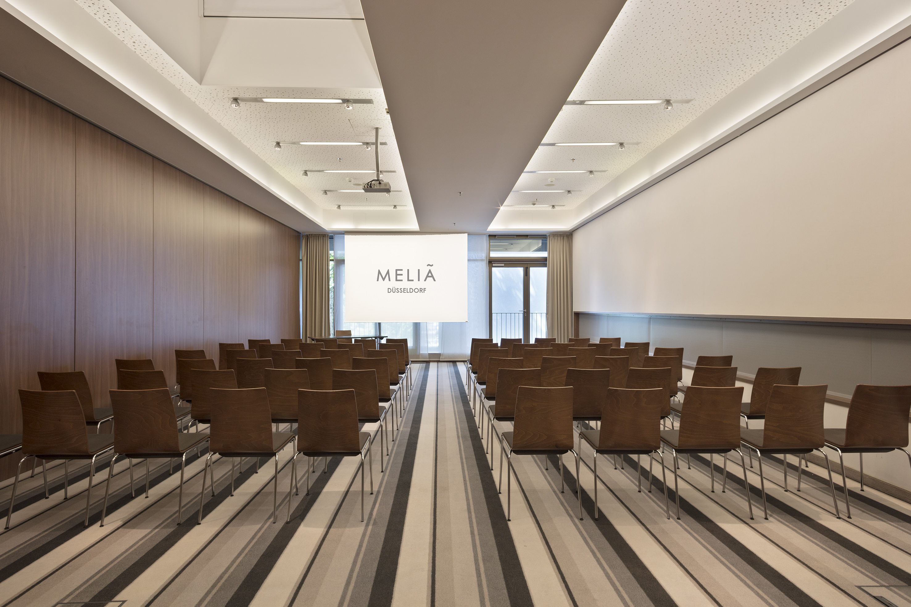 Meliã Düsseldorf conference room with rows of empty chairs and projector screen.
