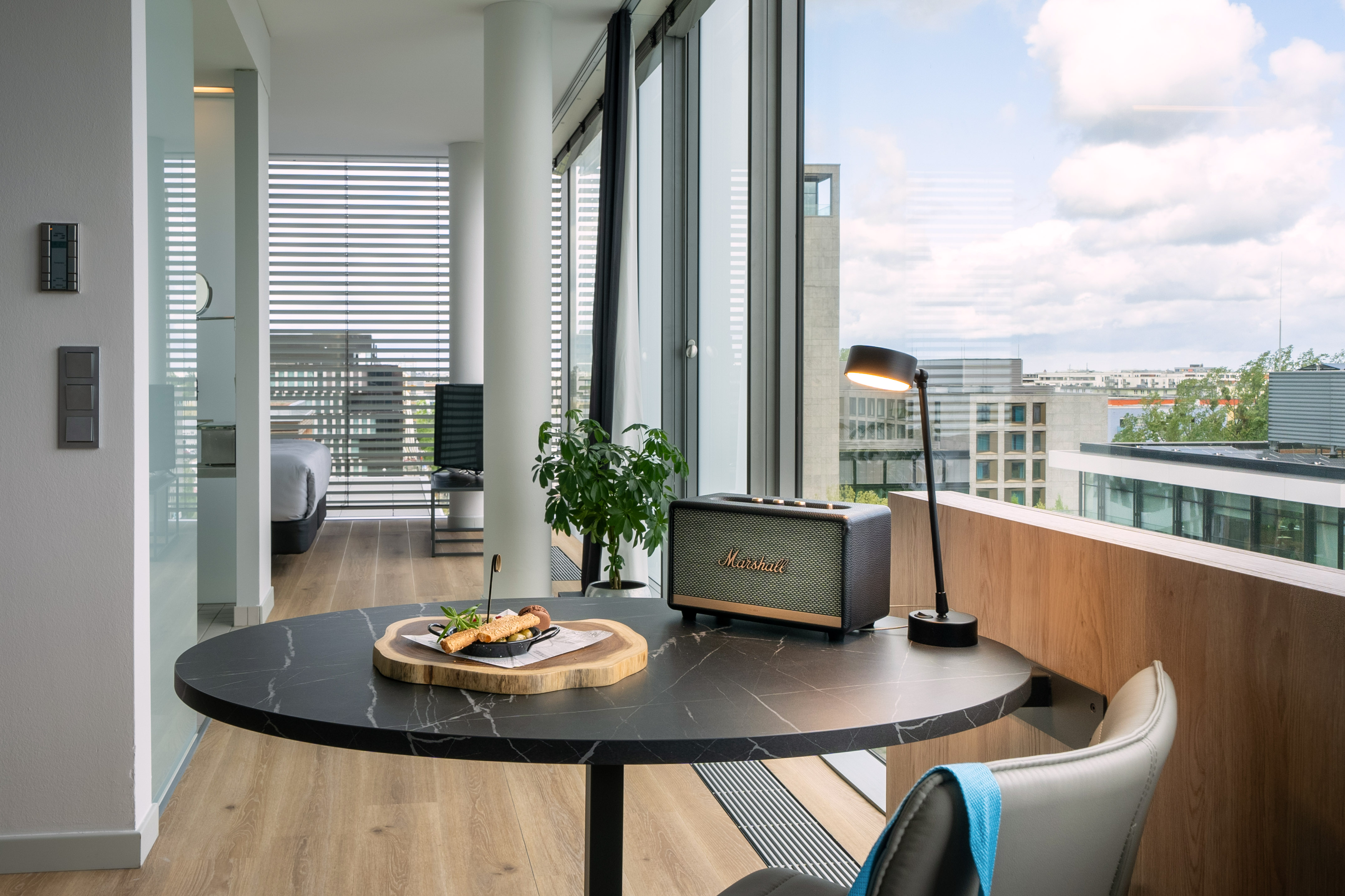 Modern apartment with black marble table, Marshall speaker, snacks, and city view.
