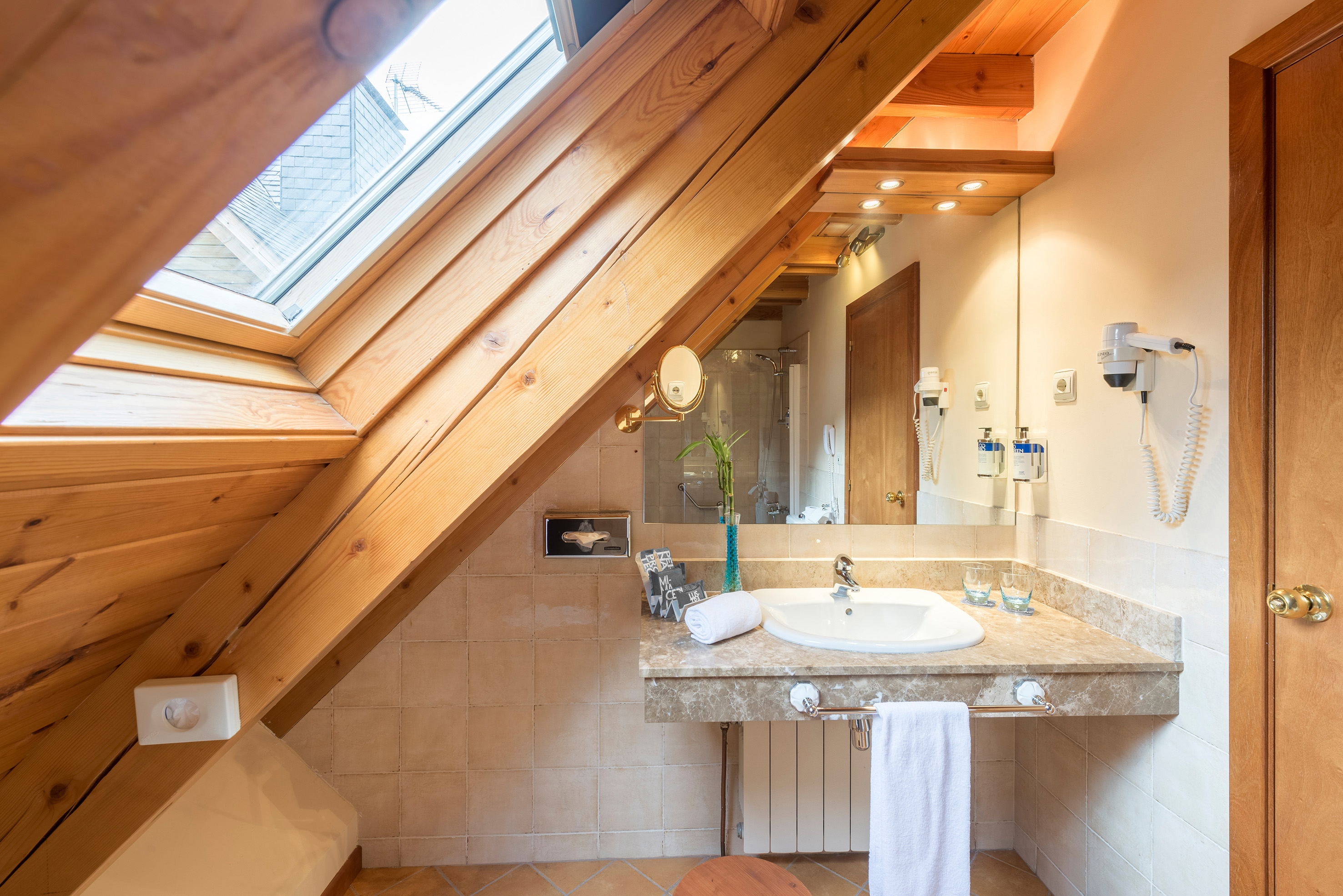 Slanted ceiling attic bathroom with skylight, wooden beams, and sink vanity.