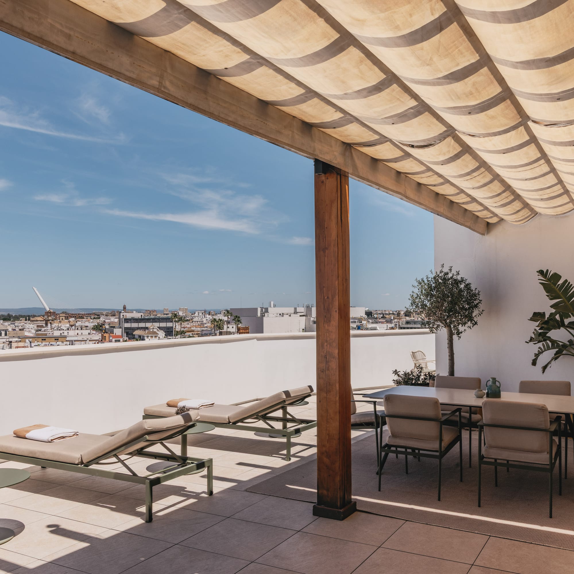 Terraza en la azotea con tumbonas, comedor, pérgola y vista urbana.