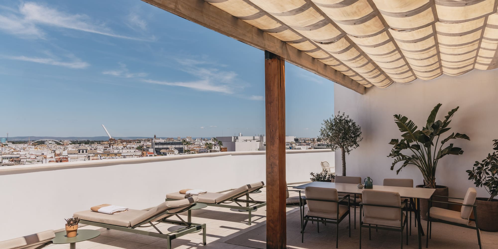 Terraza en la azotea con tumbonas, comedor, pérgola y vista urbana.