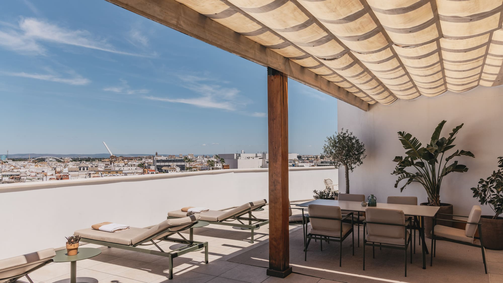 Terraza en la azotea con tumbonas, comedor, pérgola y vista urbana.