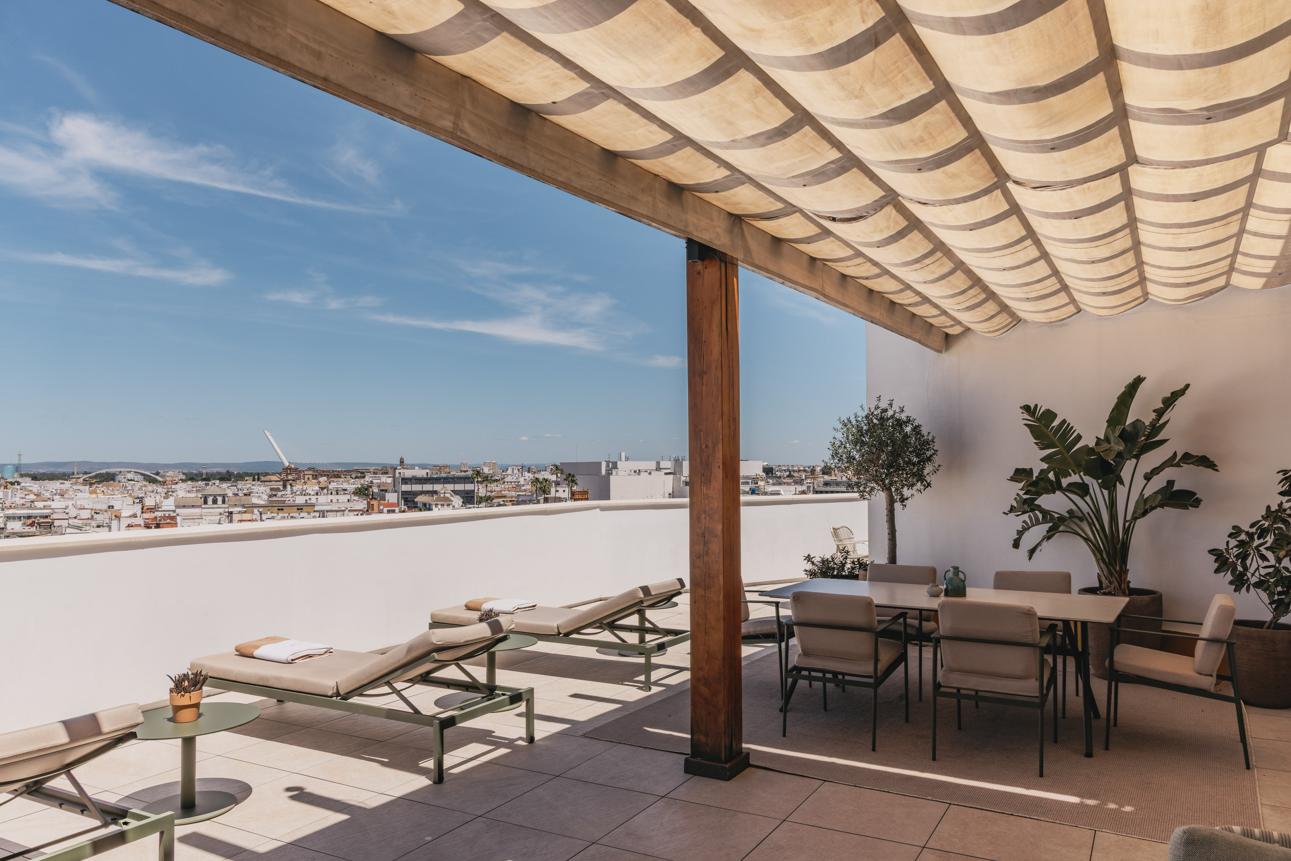 Terraza en la azotea con tumbonas, comedor, pérgola y vista urbana.