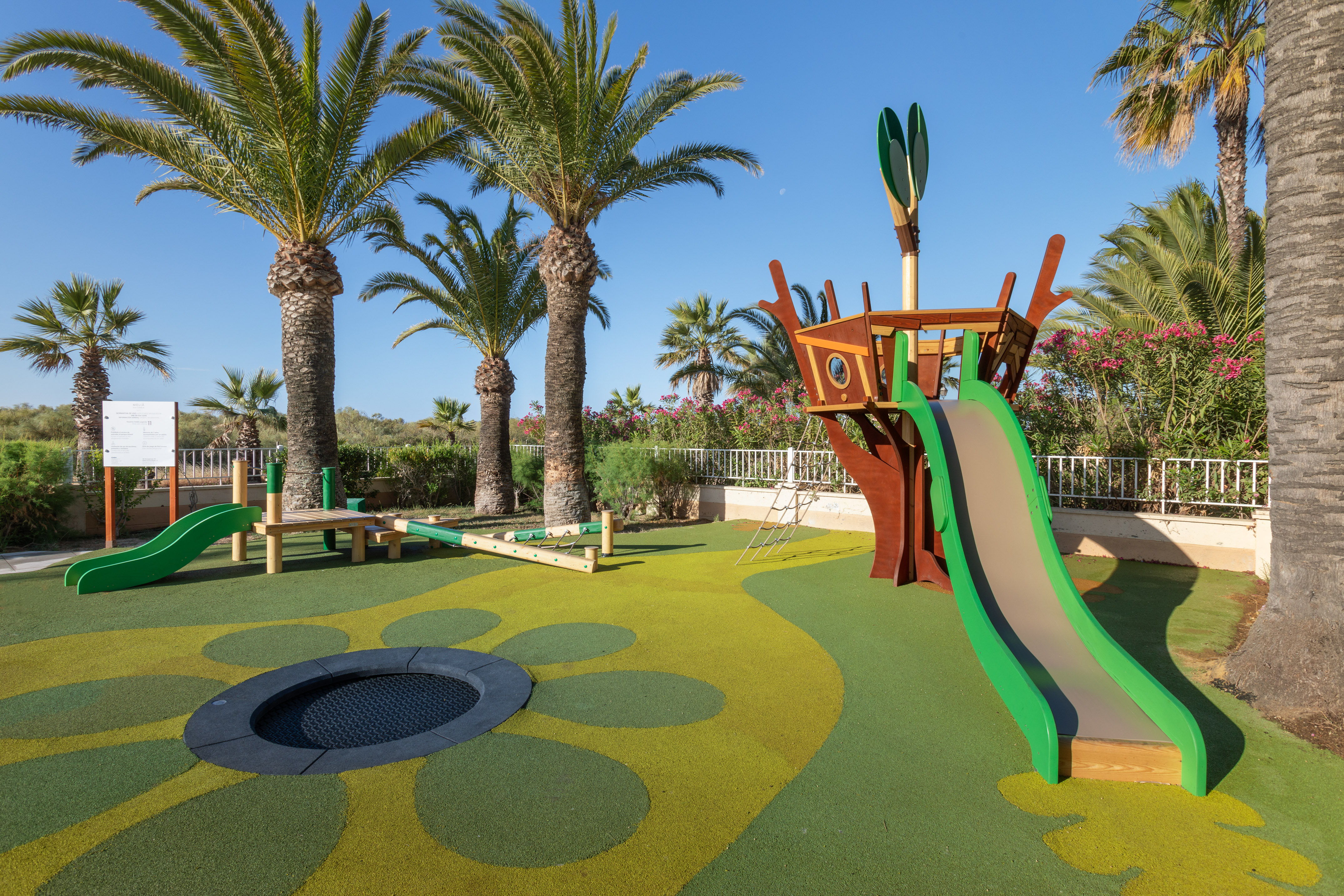 Resort playground with treehouse slide, trampoline, and palm trees.