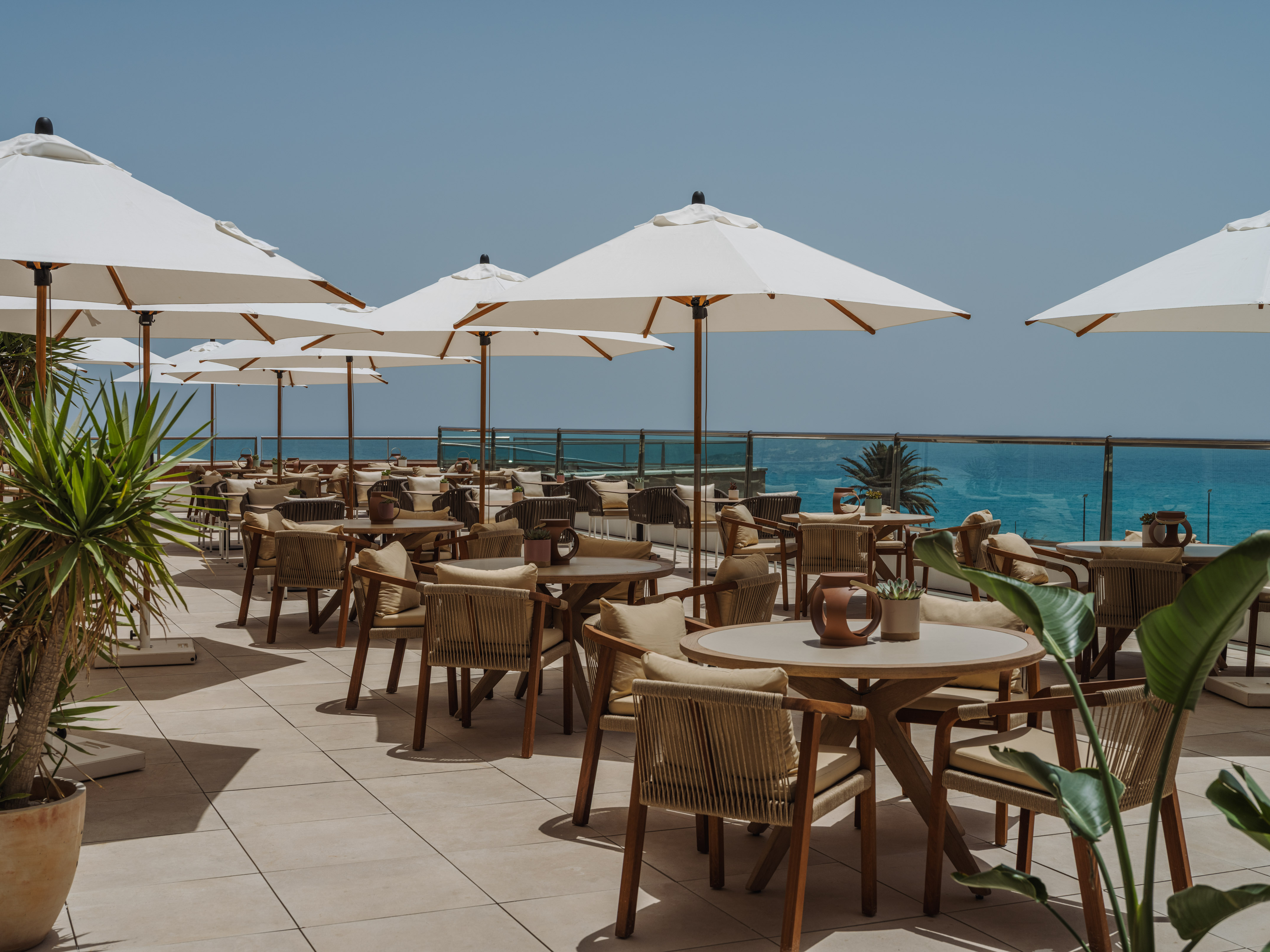 Sunny outdoor dining patio with white umbrellas and clear sea view.