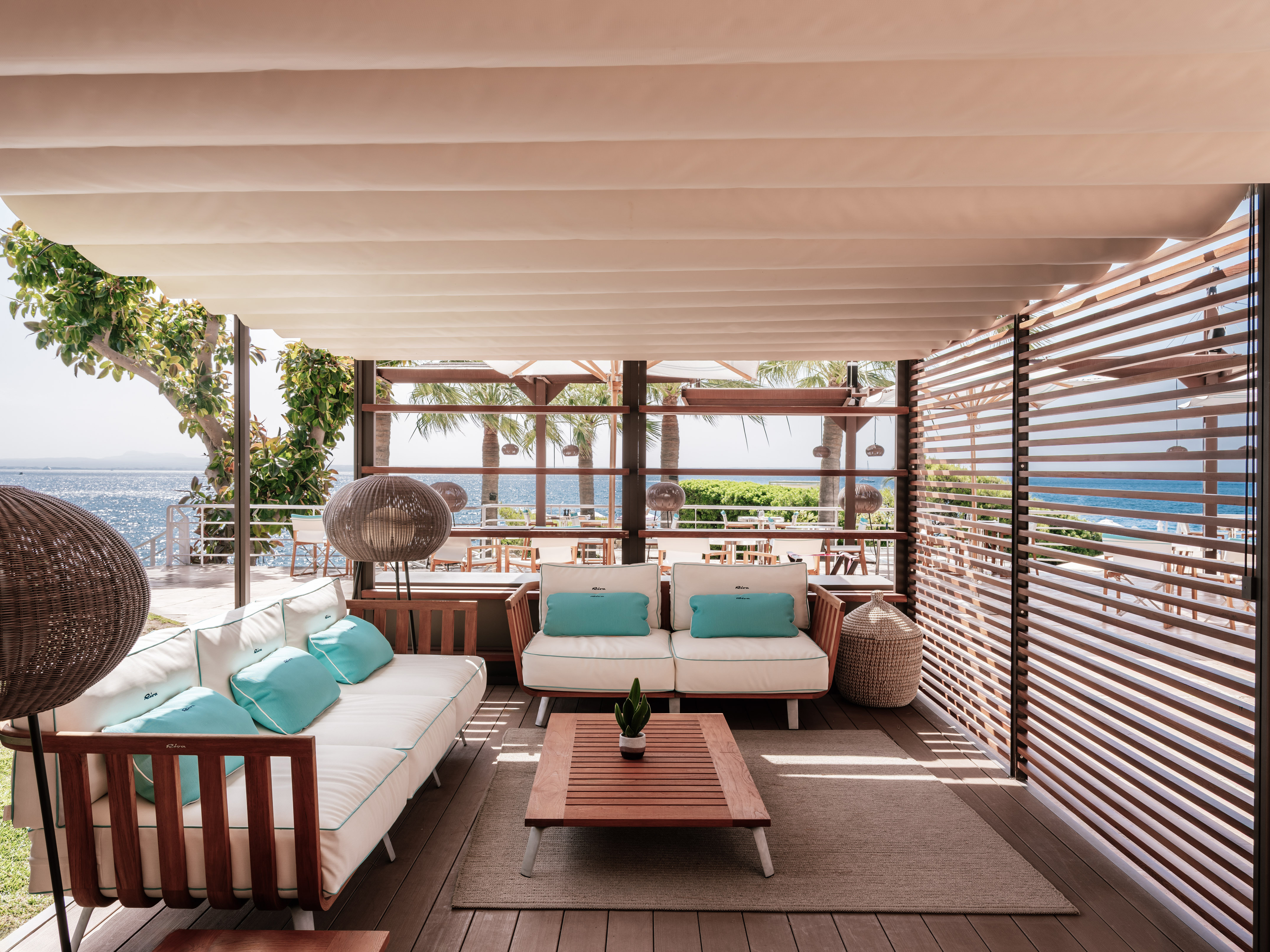 Waterfront patio lounge with white sofas, turquoise pillows, and ocean view.
