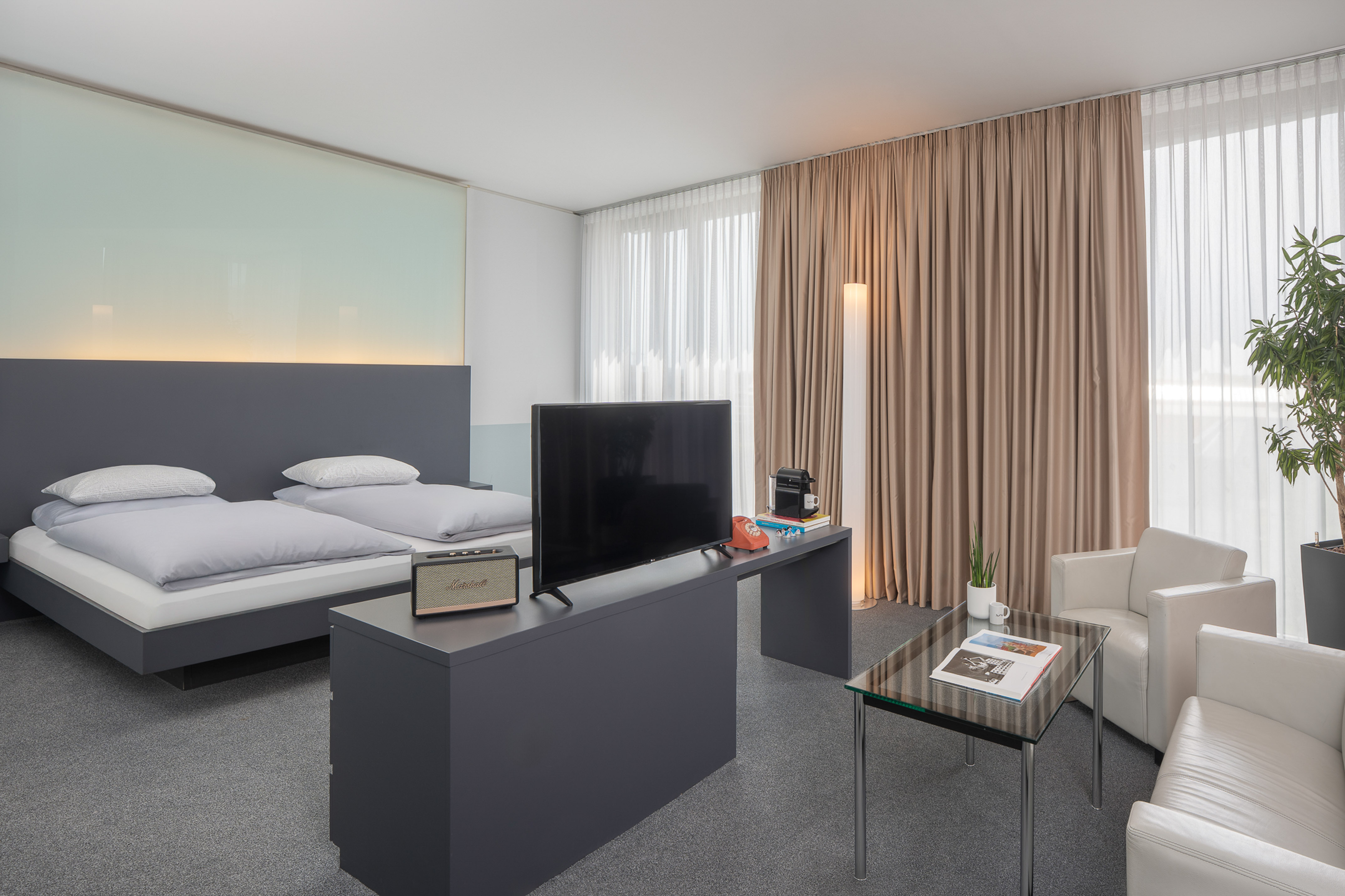 Modern hotel room with twin beds, TV, seating area, and large windows.