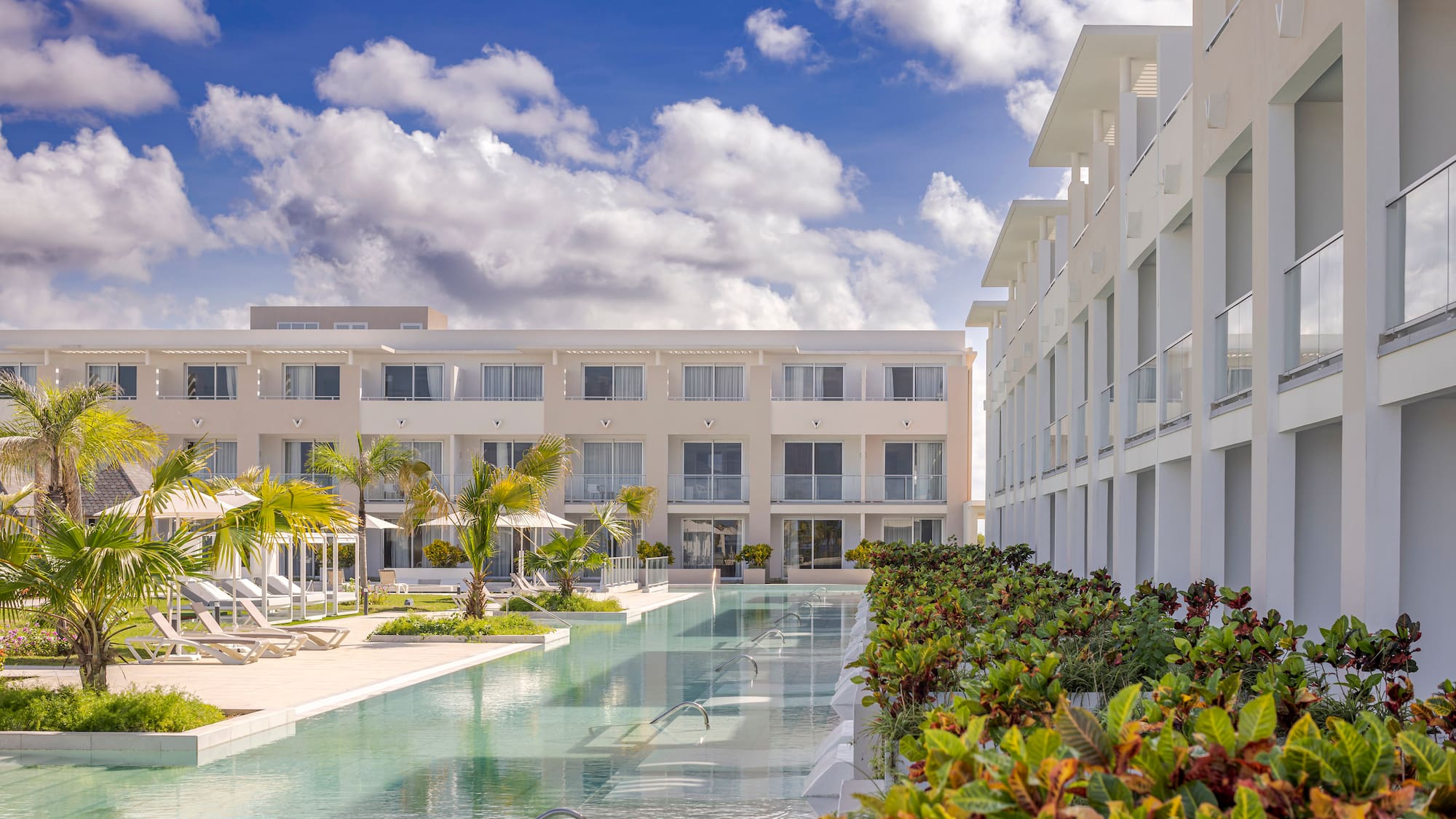 a pool with lounge chairs and trees in front of a building