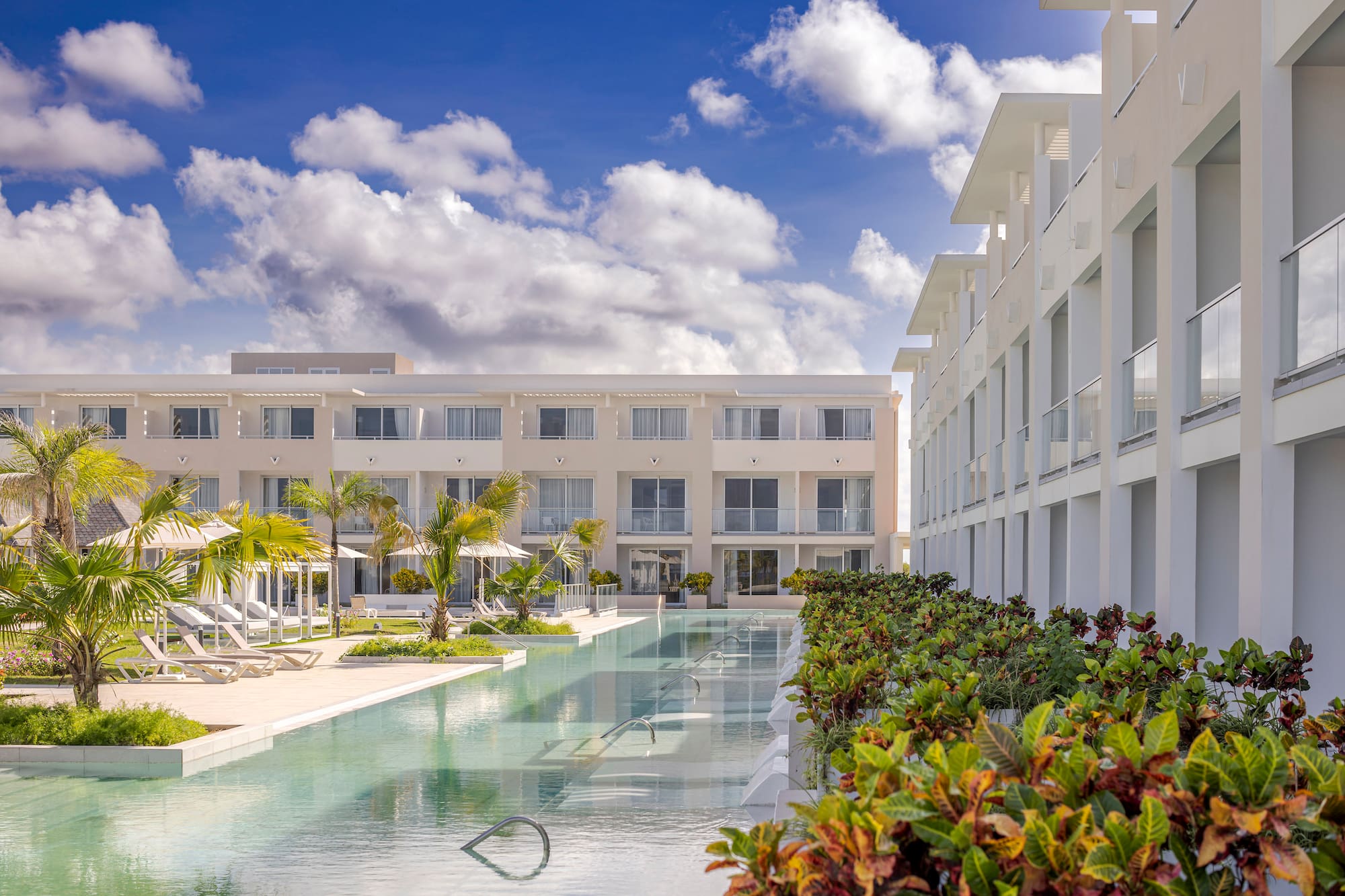 a pool with lounge chairs and trees in front of a building