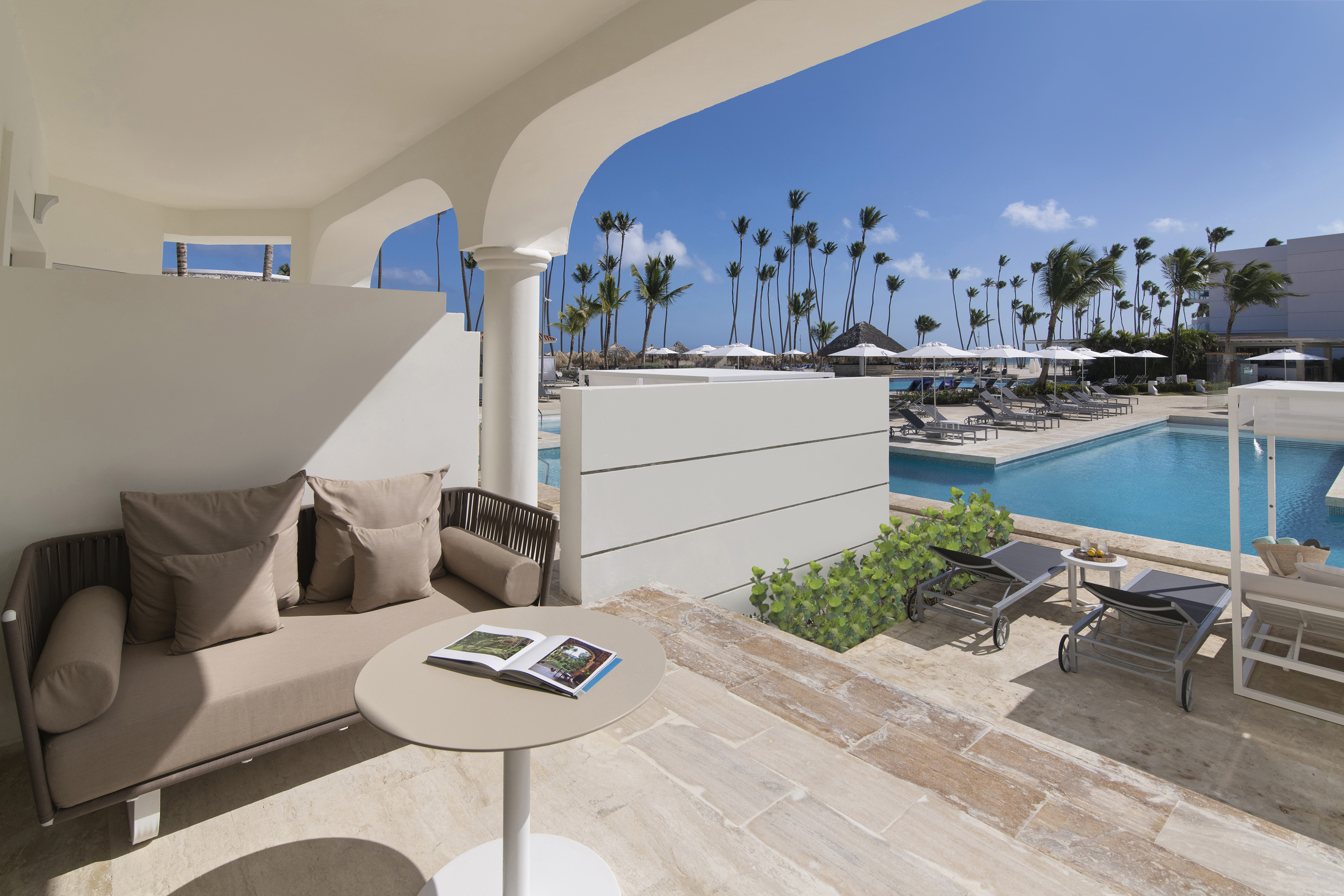 Private resort terrace with daybed, tropical pool, and palm trees.