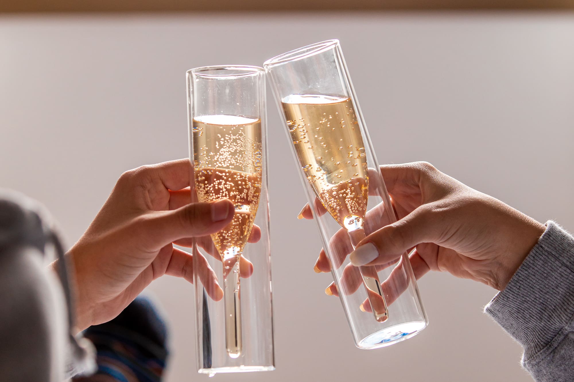 Hands toasting modern champagne flutes with sparkling wine in a relaxed setting.