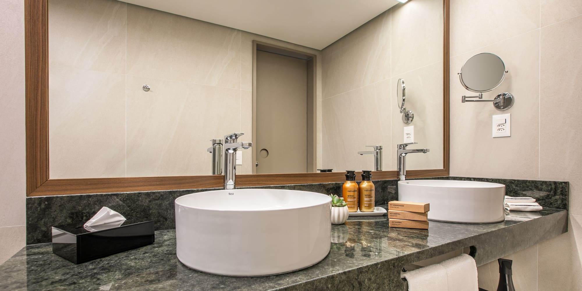 Modern hotel bathroom vanity with dual vessel sinks, green marble counter, large mirror.