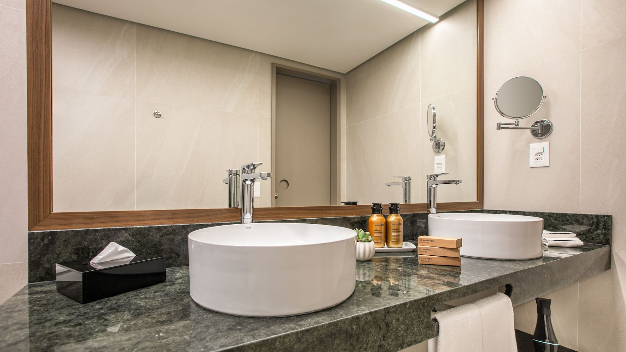 Modern hotel bathroom vanity with dual vessel sinks, green marble counter, large mirror.