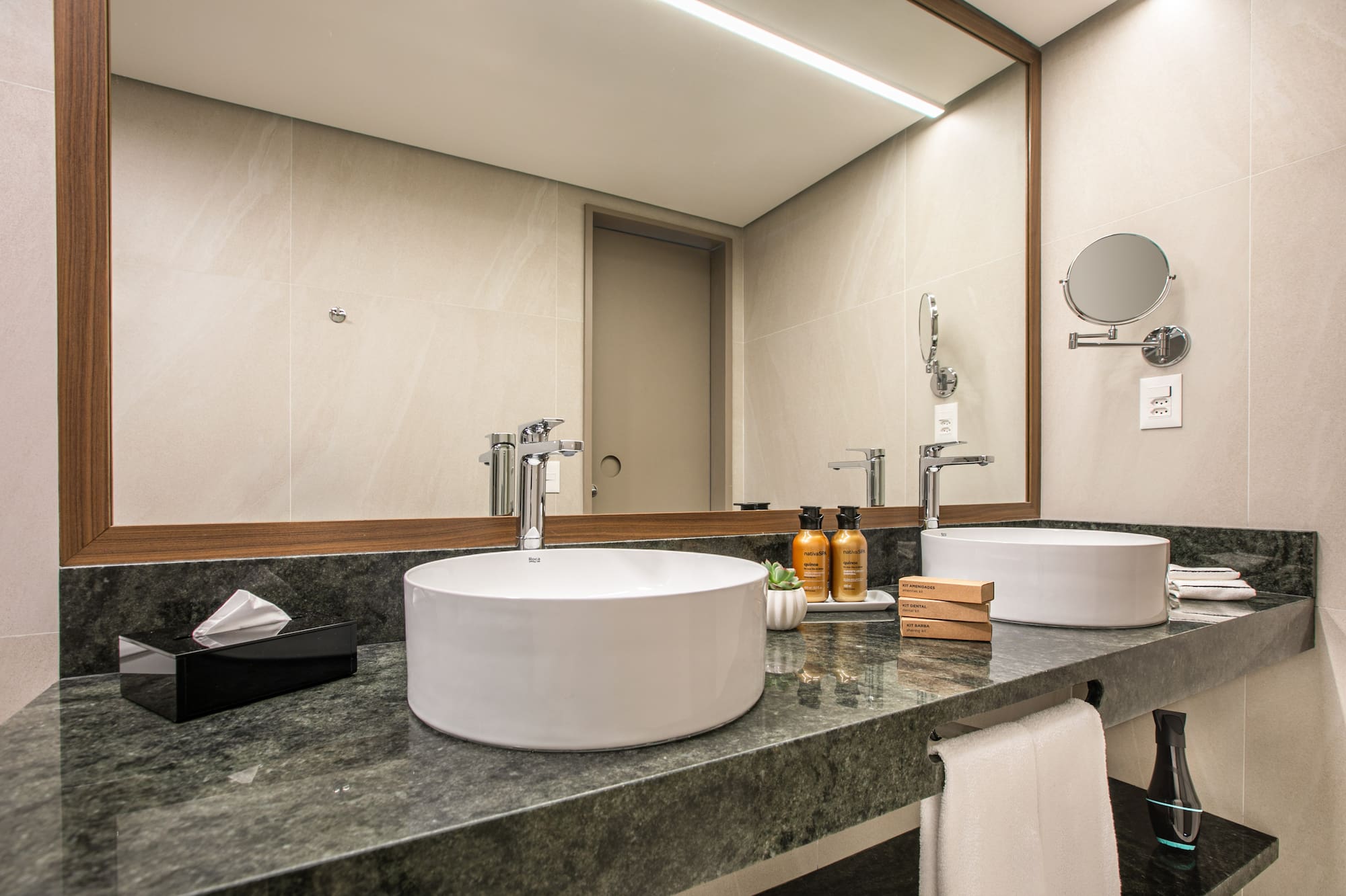 Modern hotel bathroom vanity with dual vessel sinks, green marble counter, large mirror.