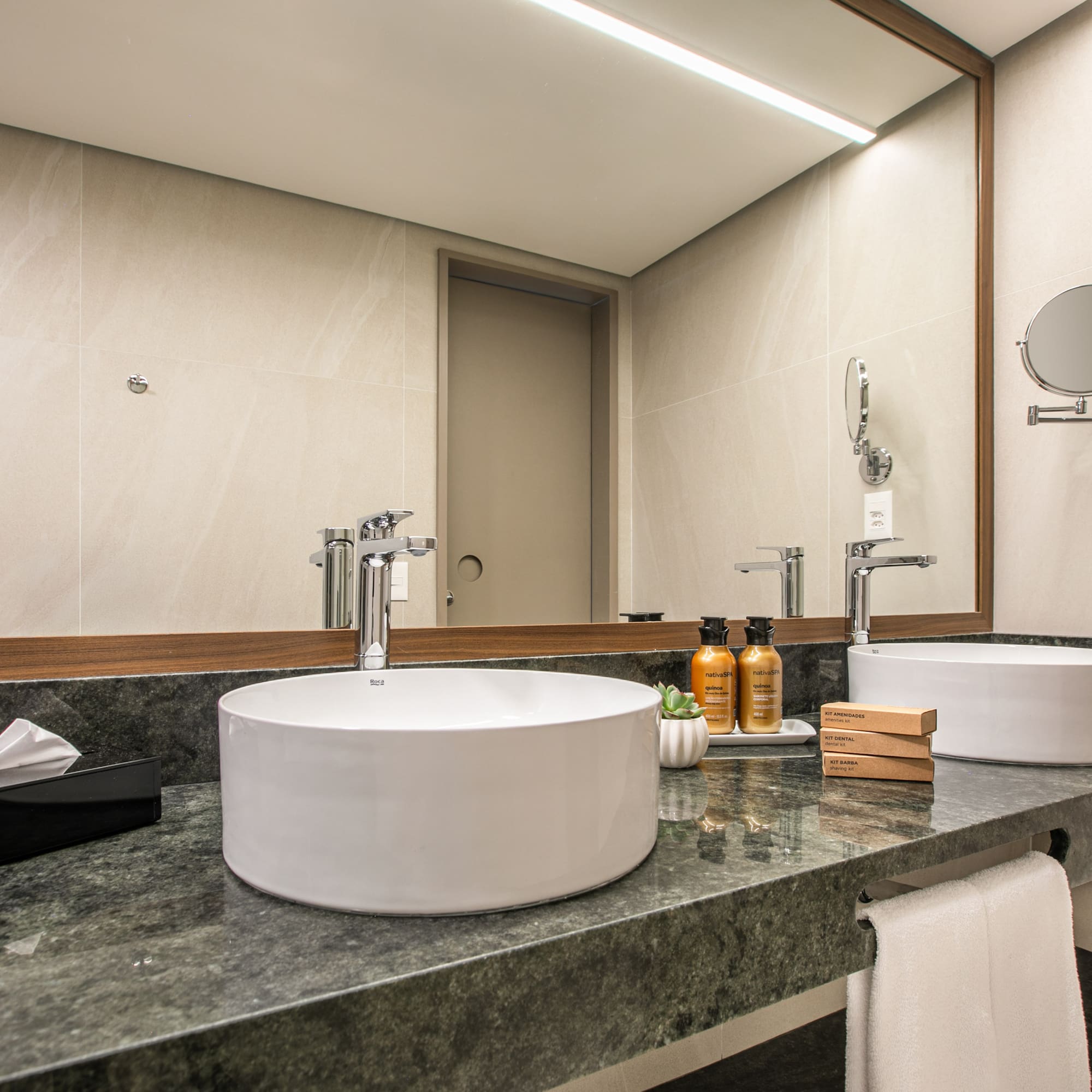 Modern hotel bathroom vanity with dual vessel sinks, green marble counter, large mirror.