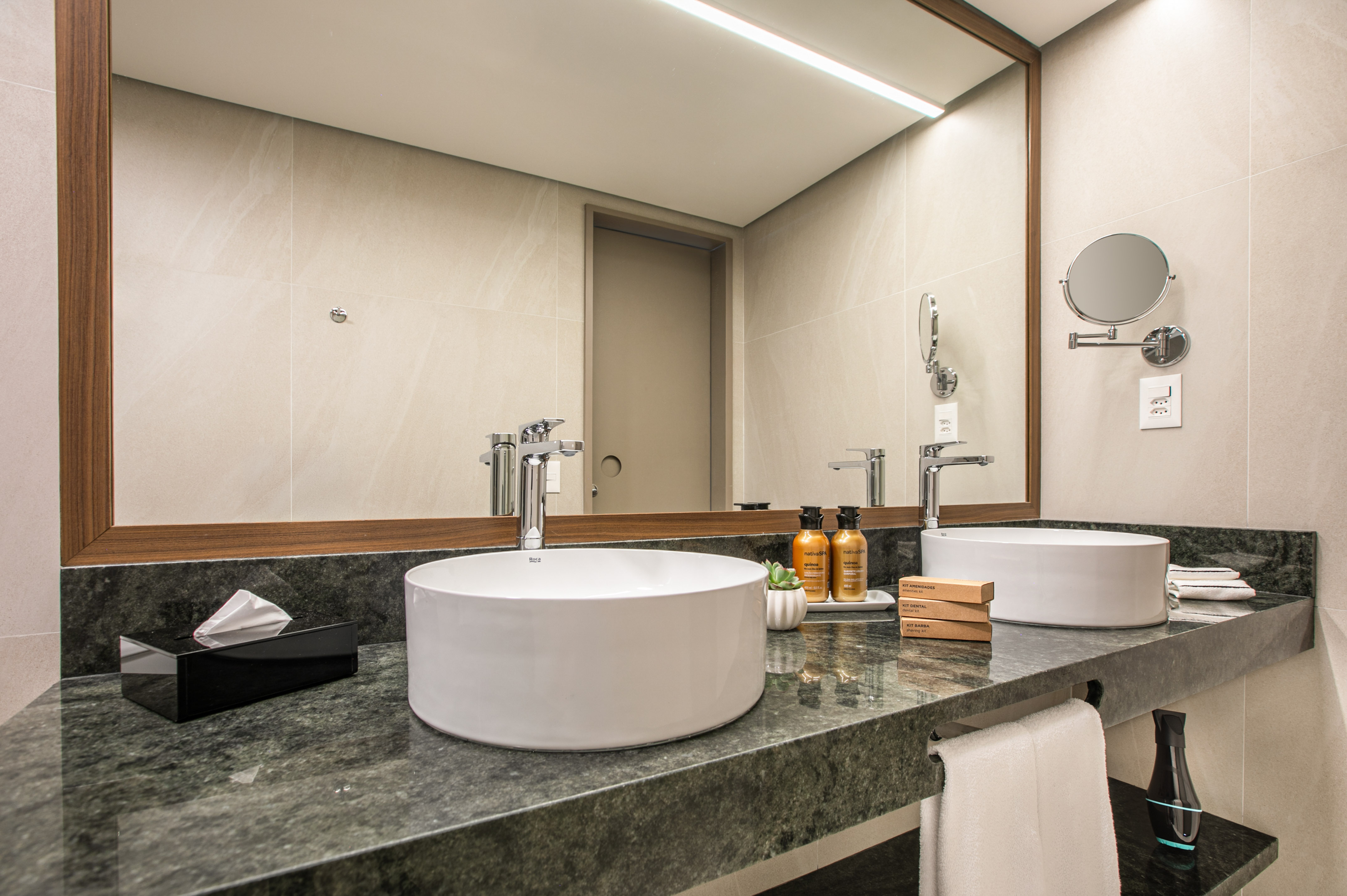 Modern hotel bathroom vanity with dual vessel sinks, green marble counter, large mirror.