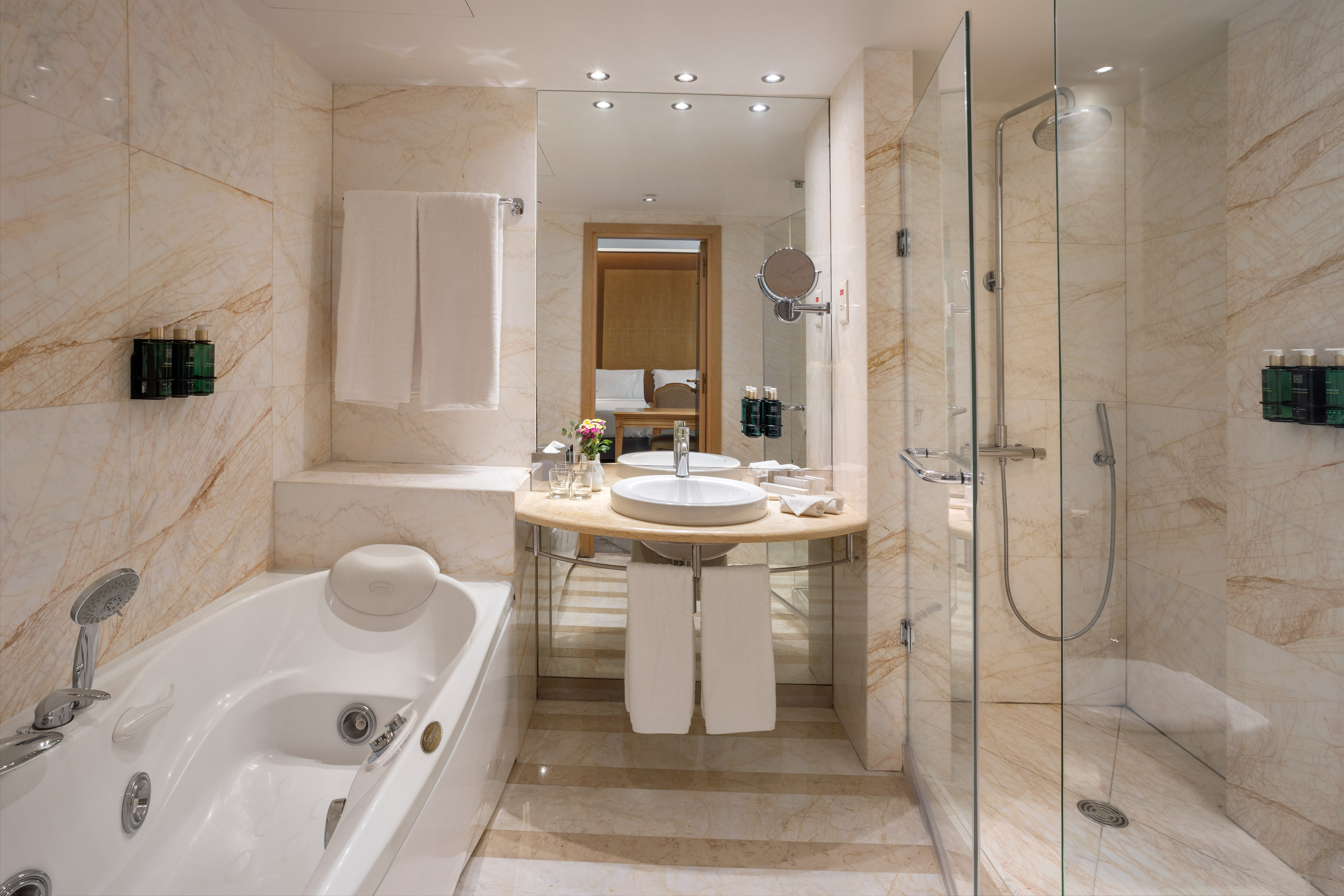 Elegant marble hotel bathroom with jetted tub, glass shower, and vanity.