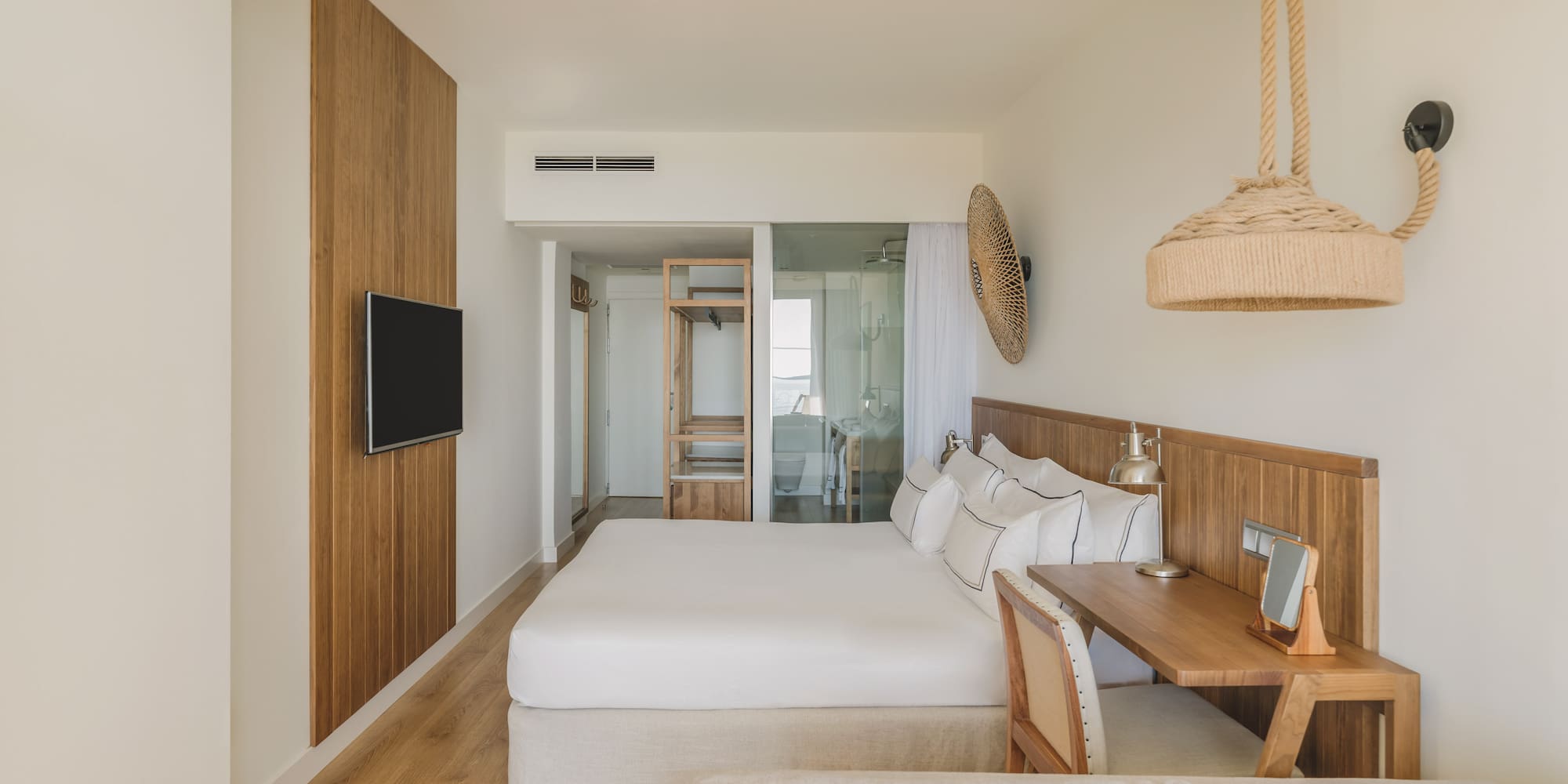 Light modern hotel bedroom with king bed, wood paneling, desk, and natural accents.