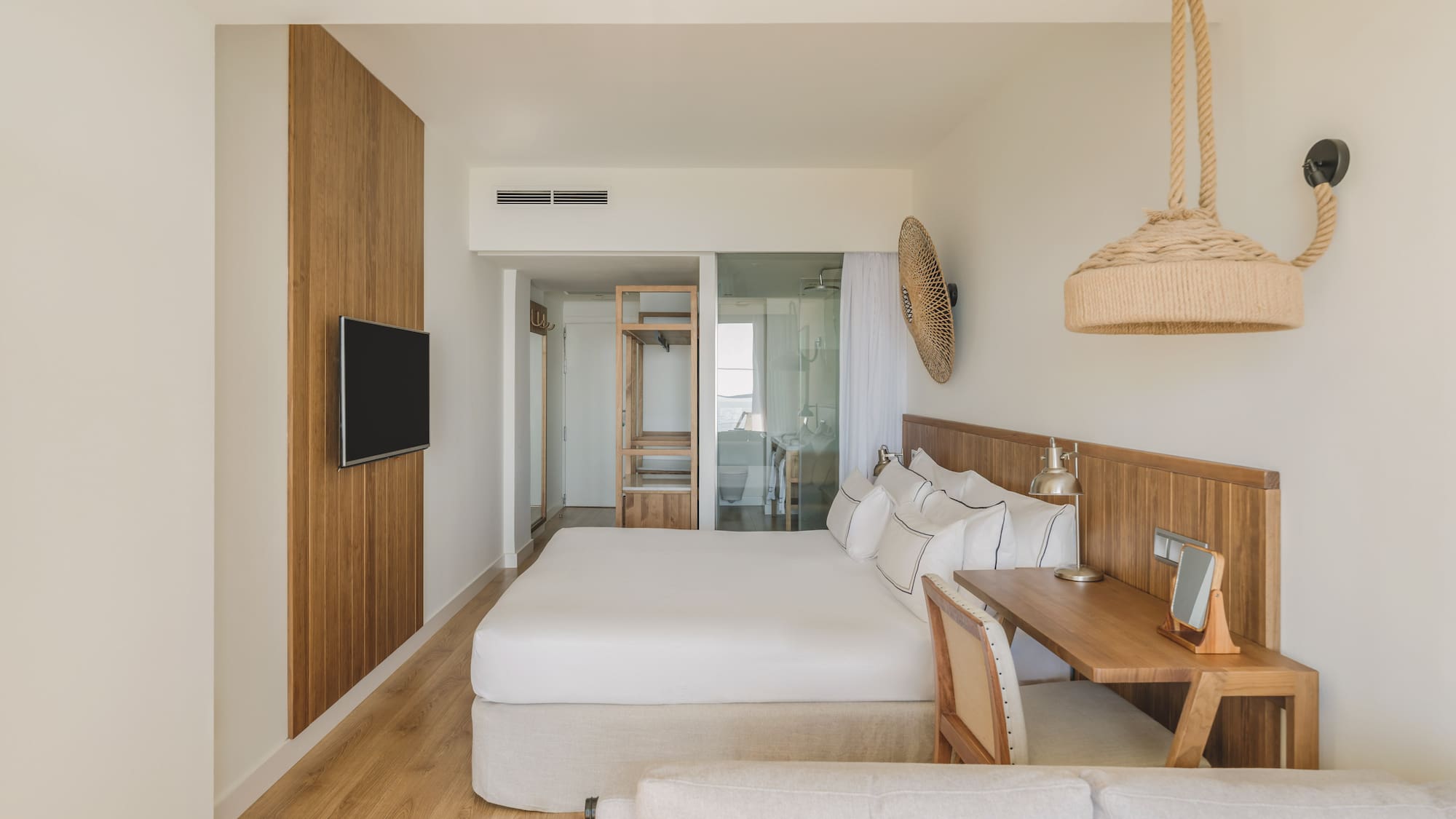 Light modern hotel bedroom with king bed, wood paneling, desk, and natural accents.