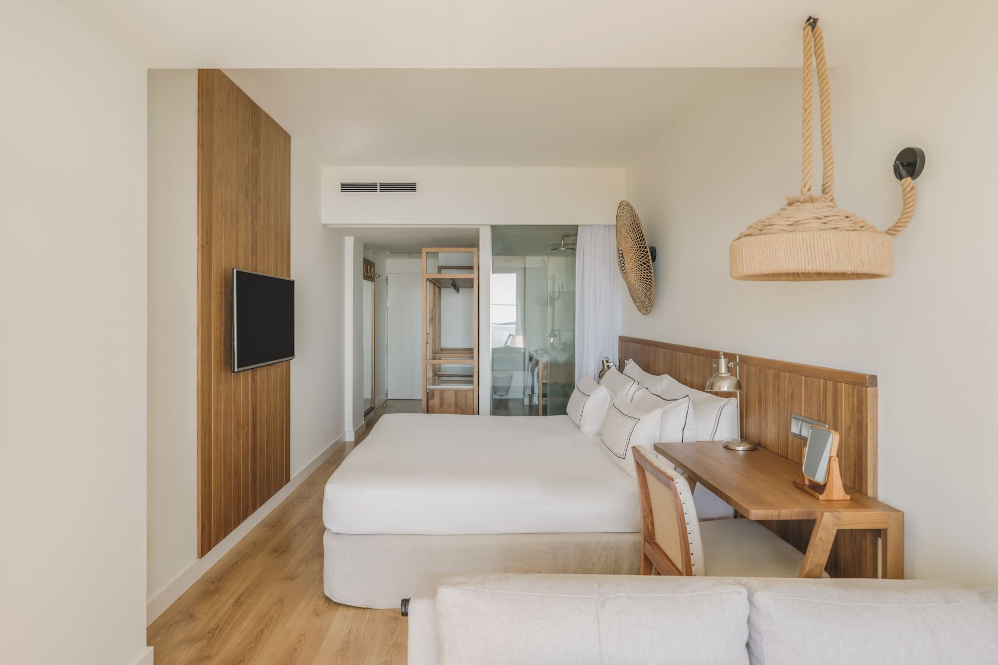 Light modern hotel bedroom with king bed, wood paneling, desk, and natural accents.