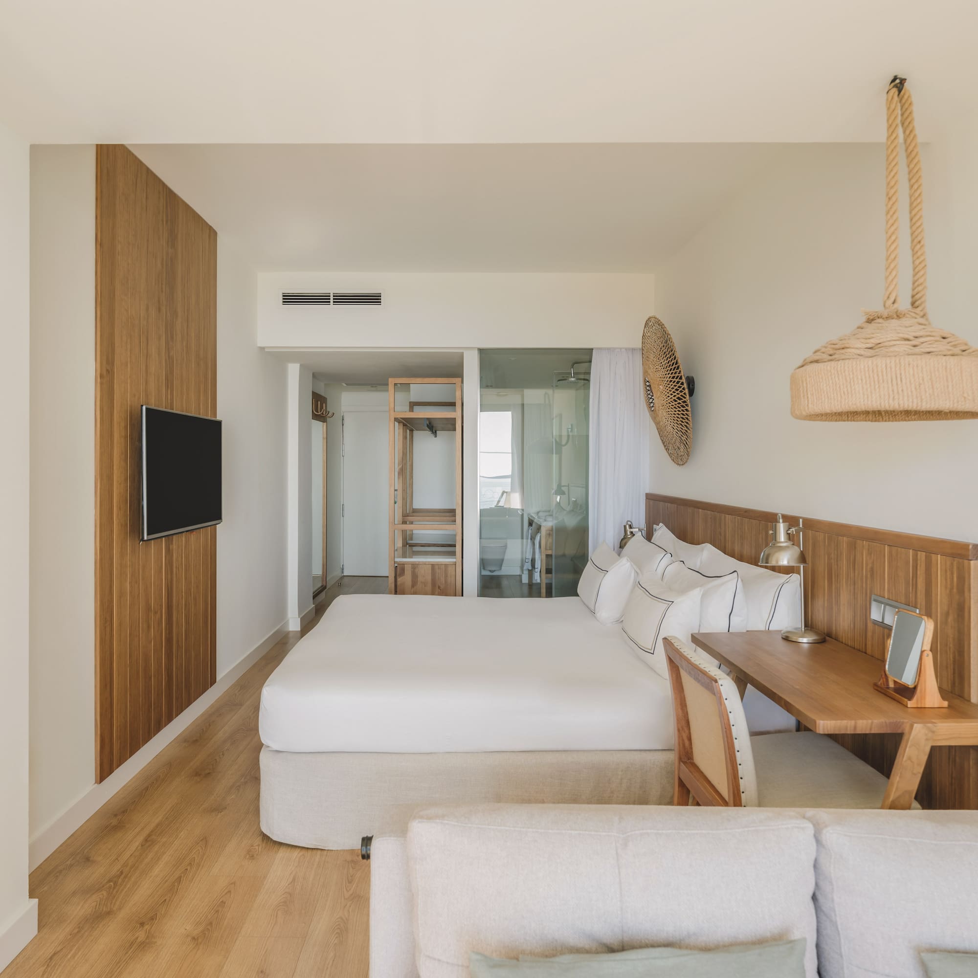 Light modern hotel bedroom with king bed, wood paneling, desk, and natural accents.