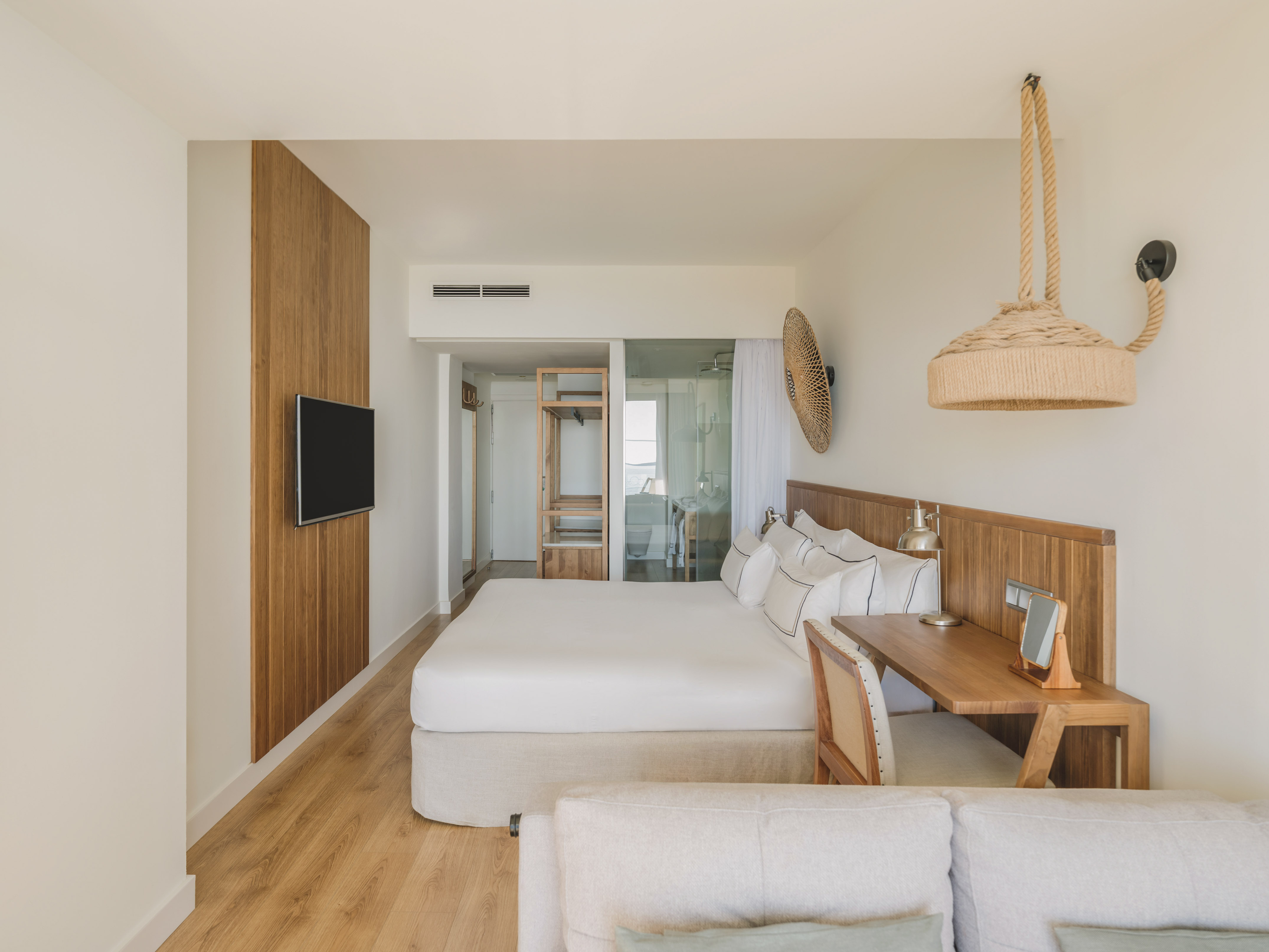 Light modern hotel bedroom with king bed, wood paneling, desk, and natural accents.