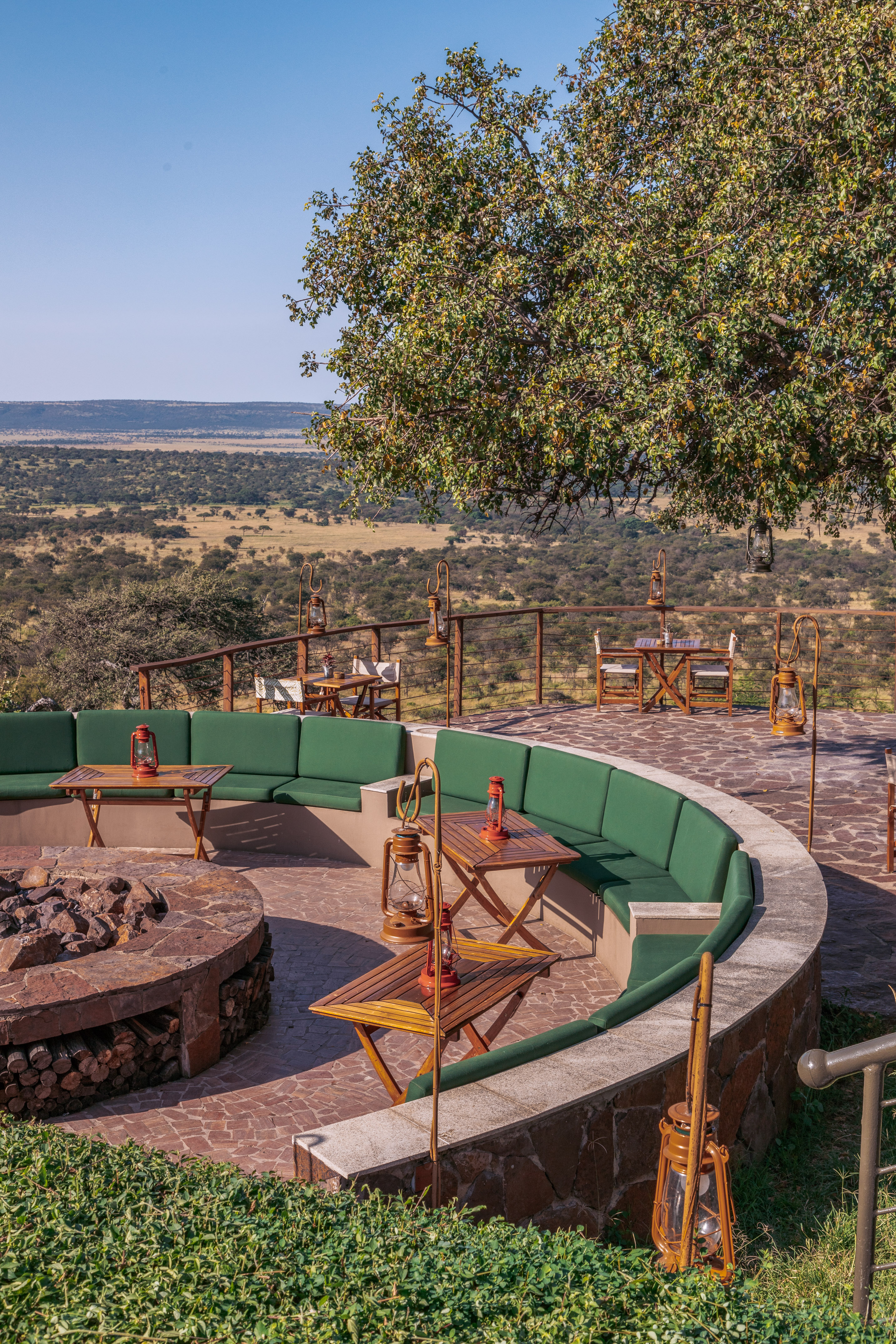 Outdoor safari lodge fire pit area with green seating overlooking savanna plains.