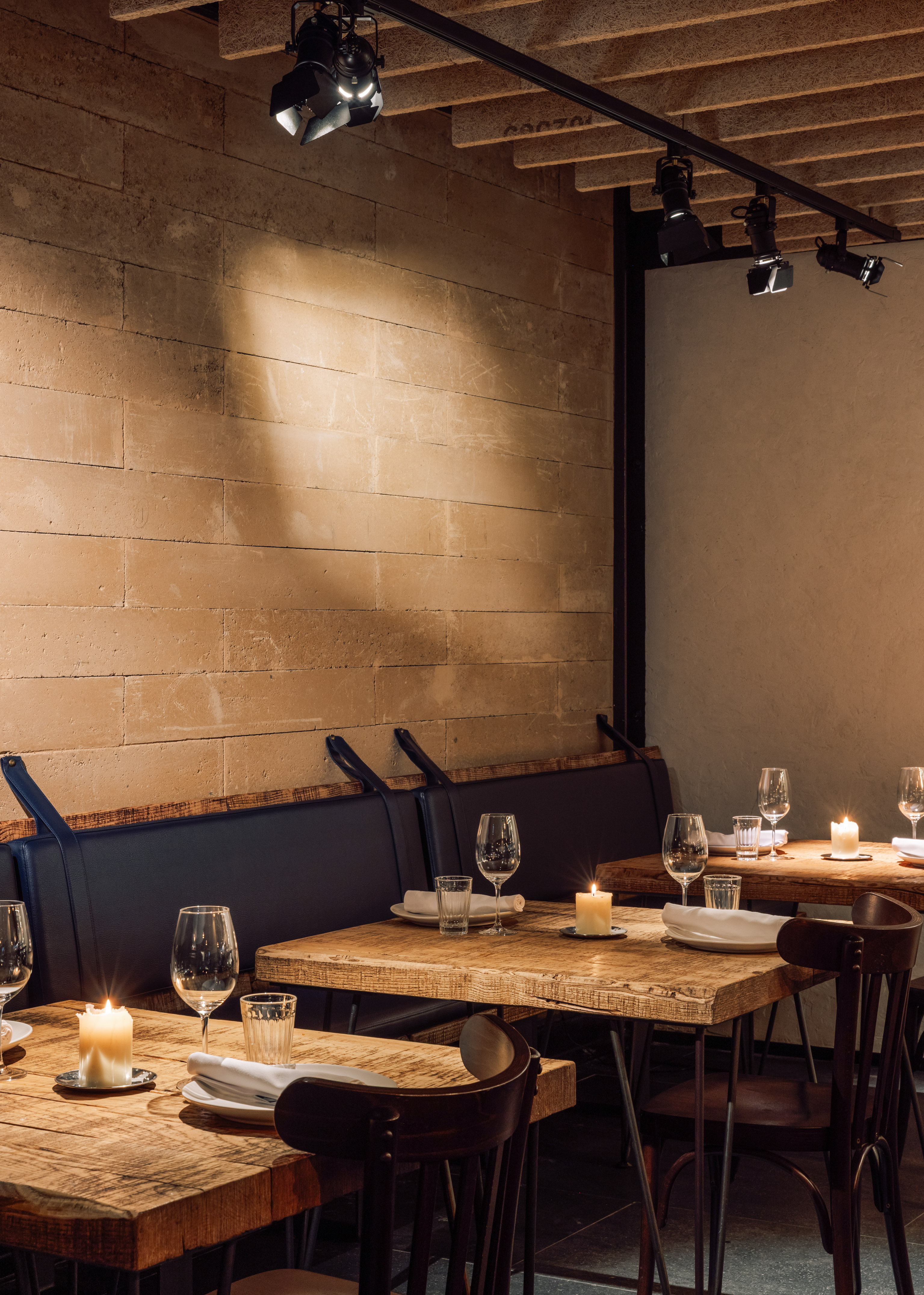 Cozy restaurant interior with candlelit wooden tables, blue banquette, and brick wall.