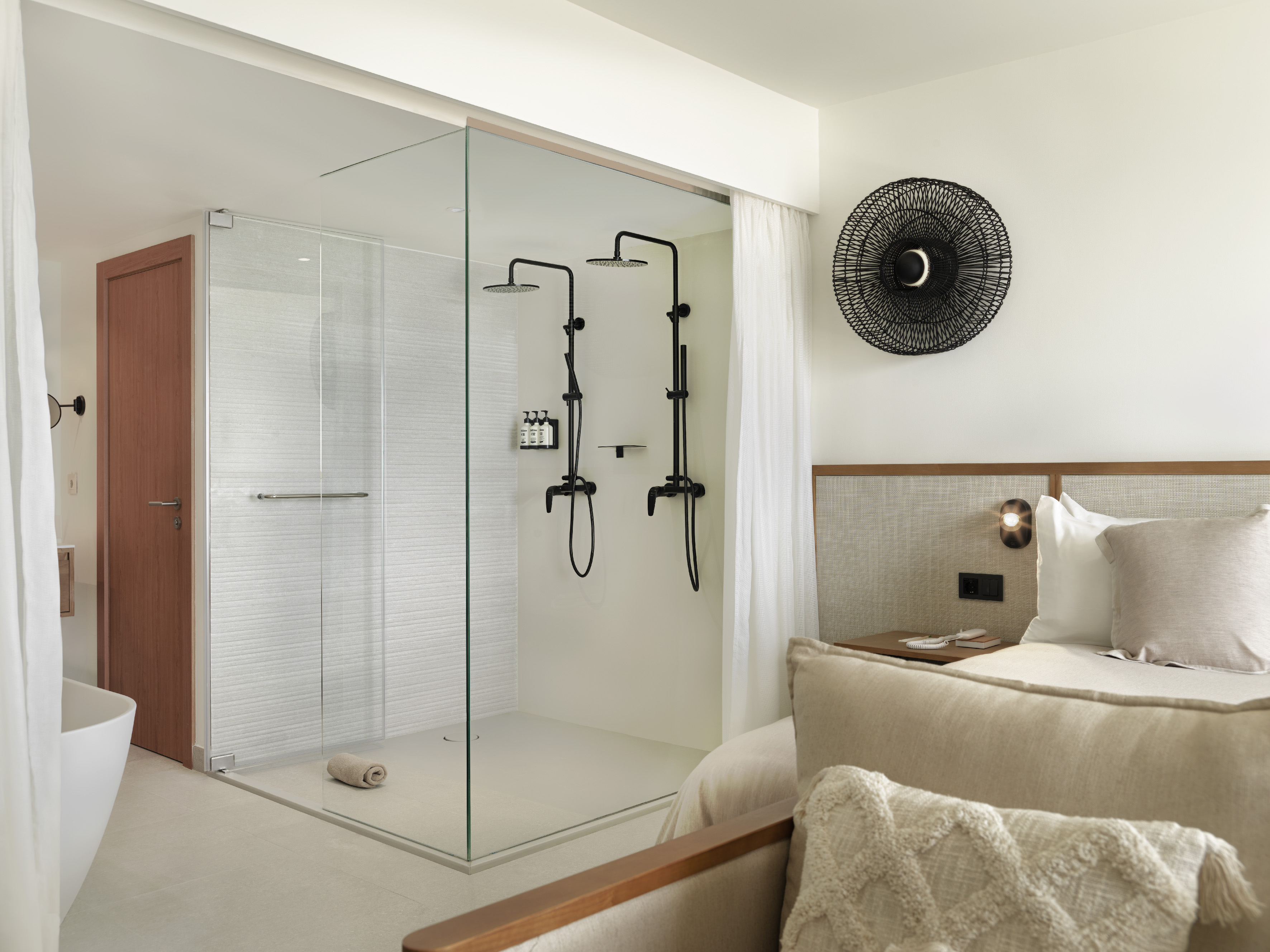 Modern hotel suite with glass shower, dual black fixtures, and bedroom.
