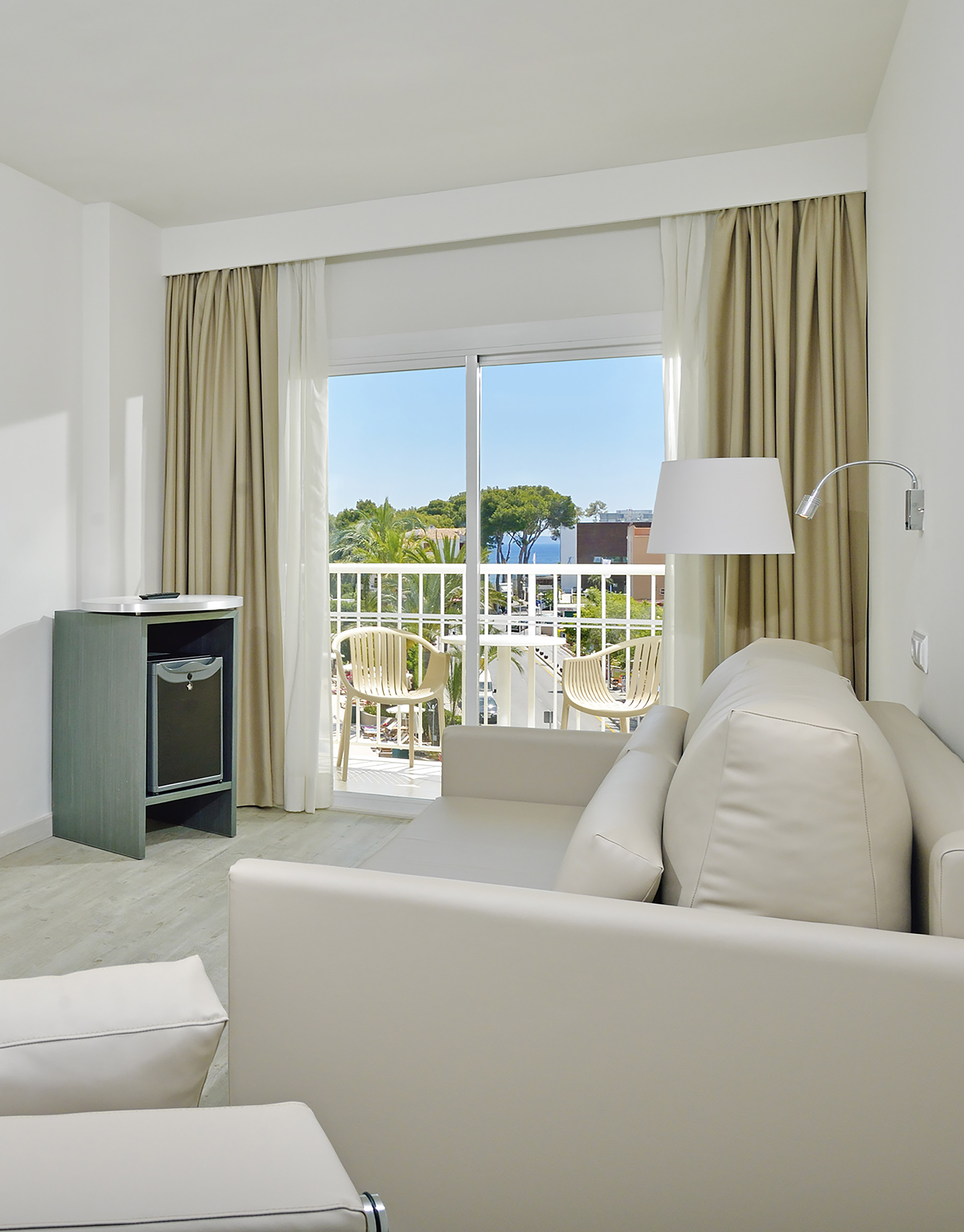 Modern hotel room with white sofa, balcony, and ocean view.