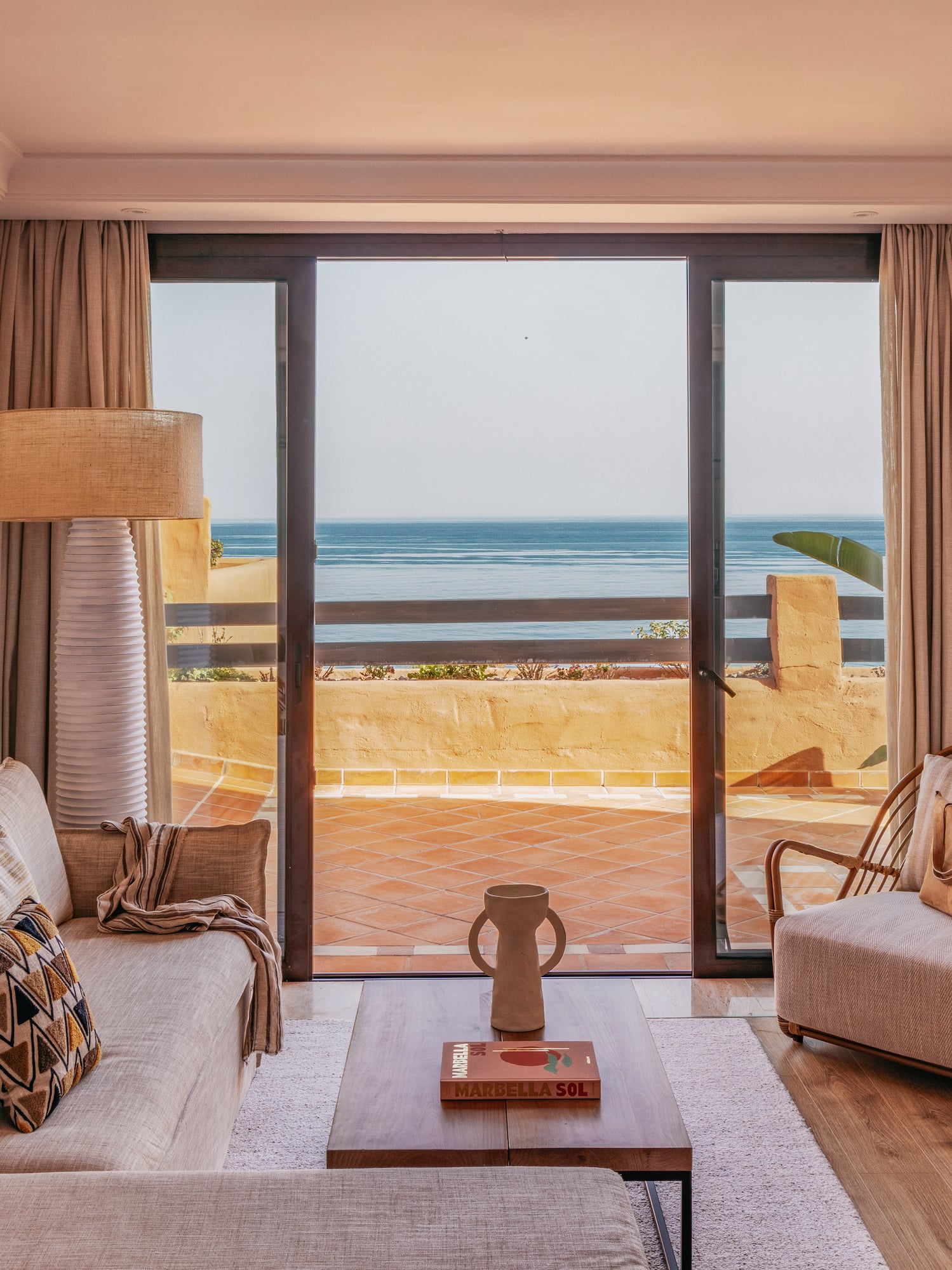 Marbella living room: ocean view balcony, sofa, and rattan armchair.
