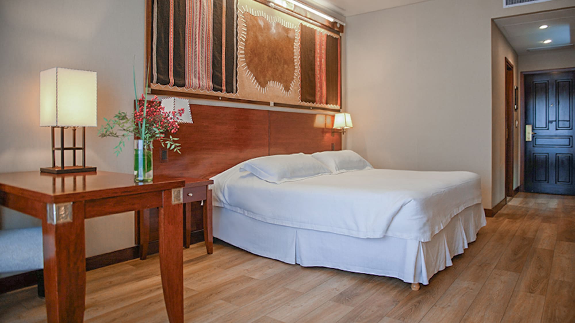 a bed with a wood headboard and a table with a vase of flowers