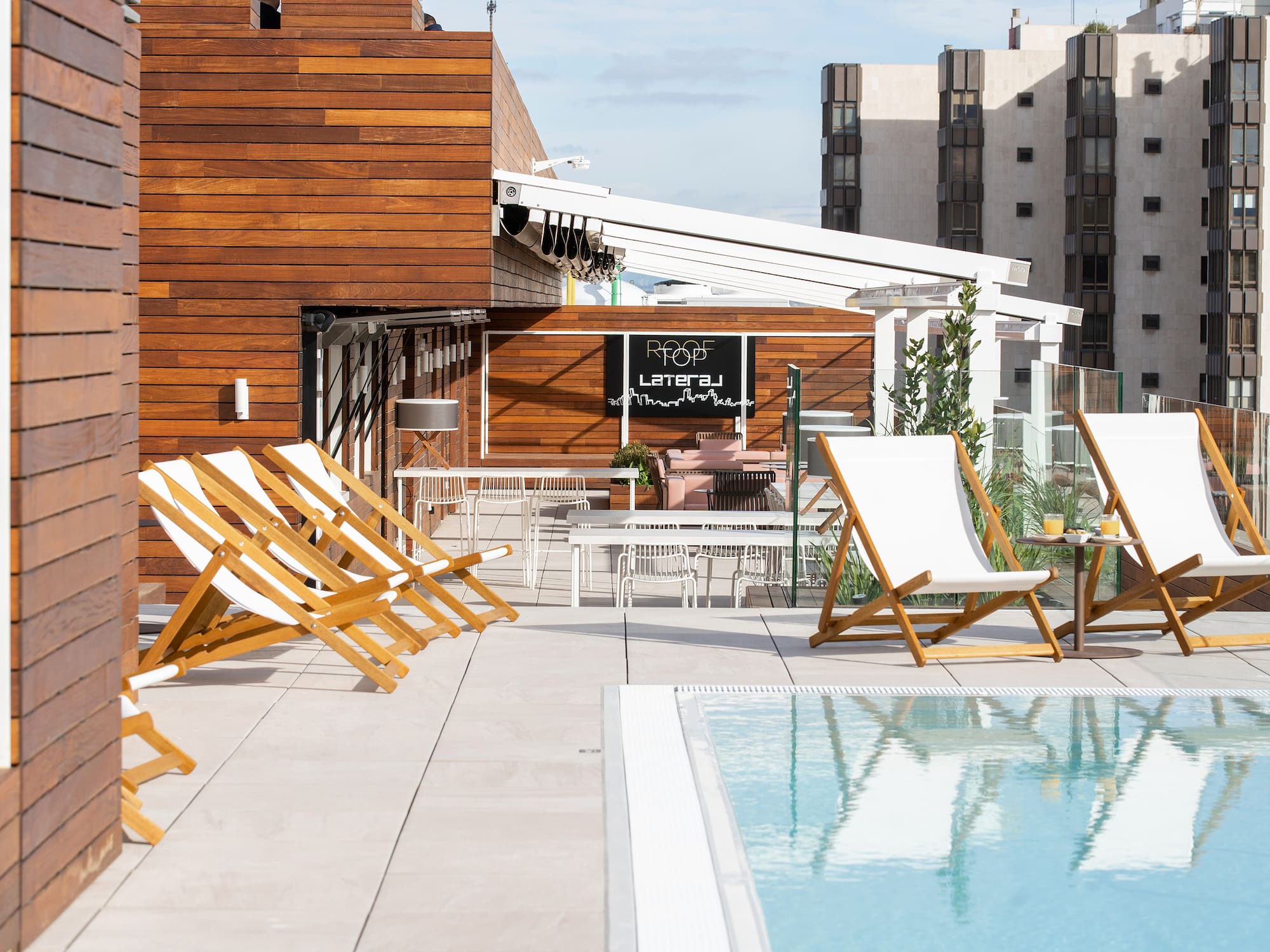 Modern rooftop bar with pool, wood paneling, and lounge chairs.