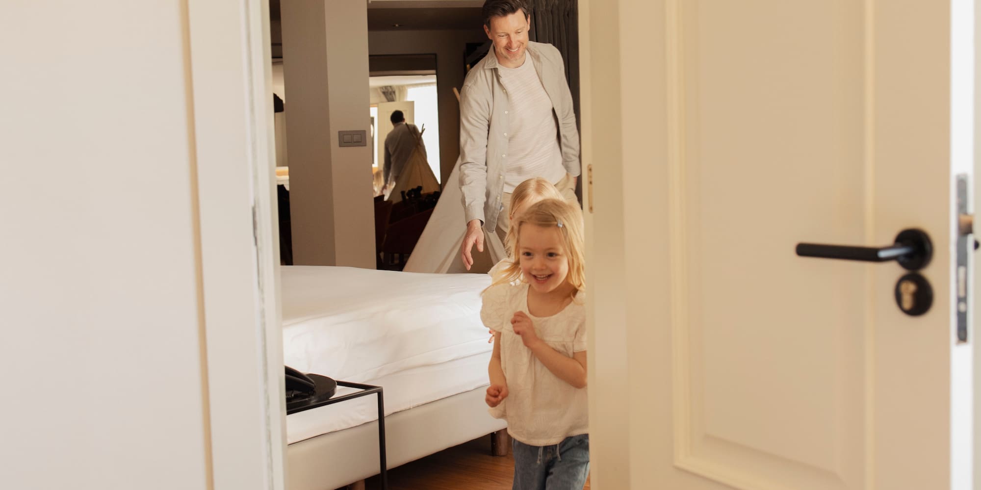 Happy blonde girl and father running through a bright bedroom doorway.