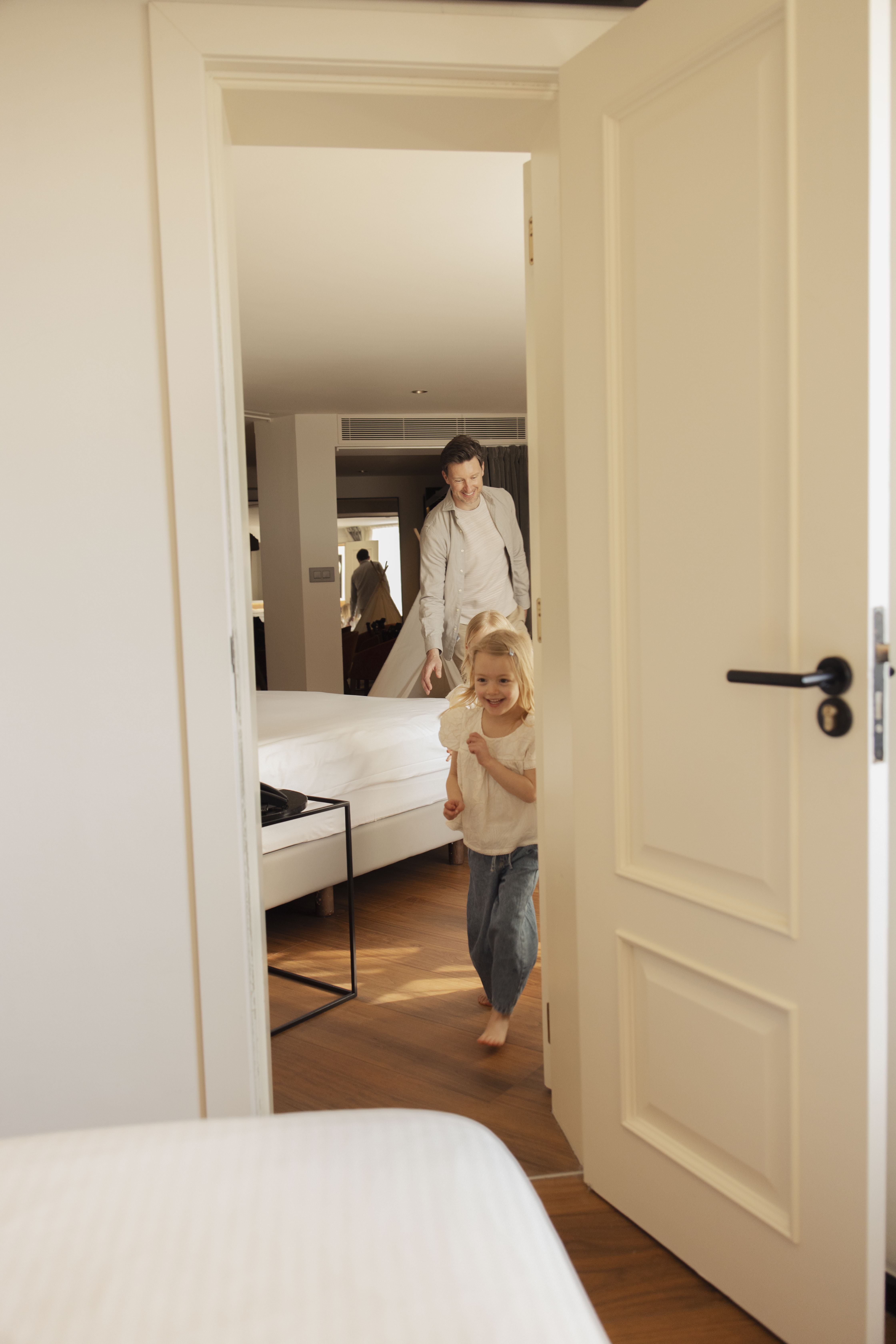 Happy blonde girl and father running through a bright bedroom doorway.