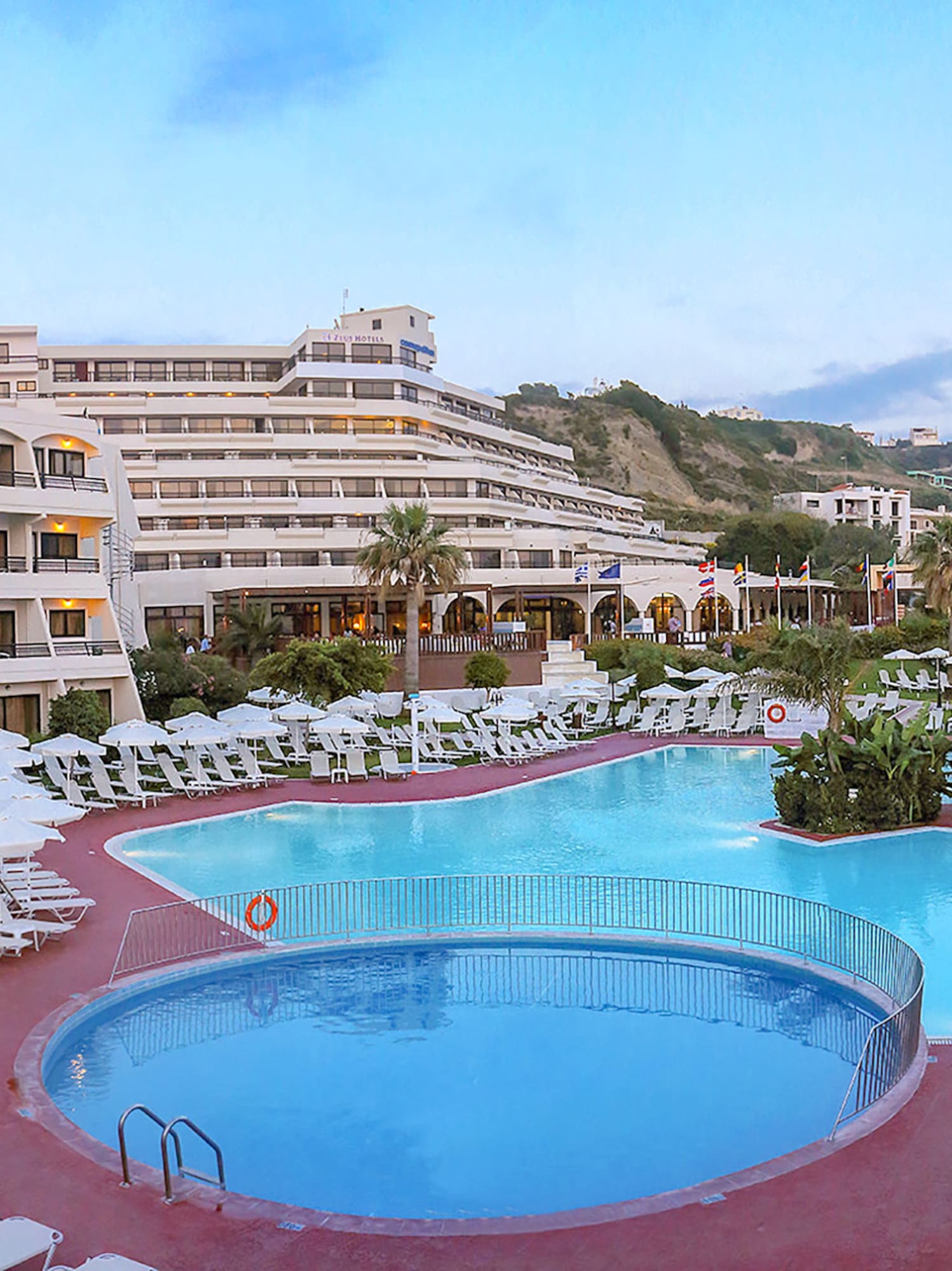 a pool with chairs and umbrellas in front of a hotel