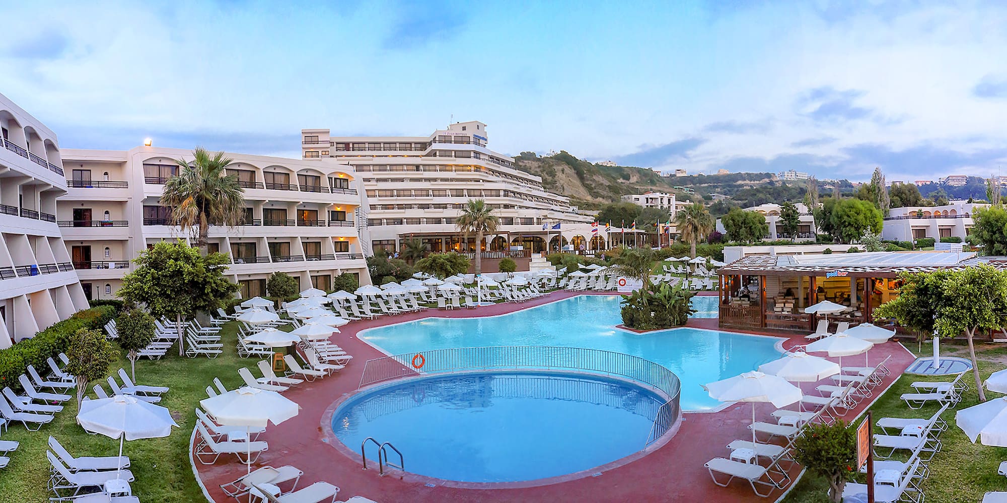 a pool with chairs and umbrellas in front of a hotel