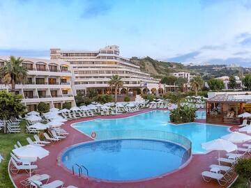 a pool with chairs and umbrellas in front of a hotel