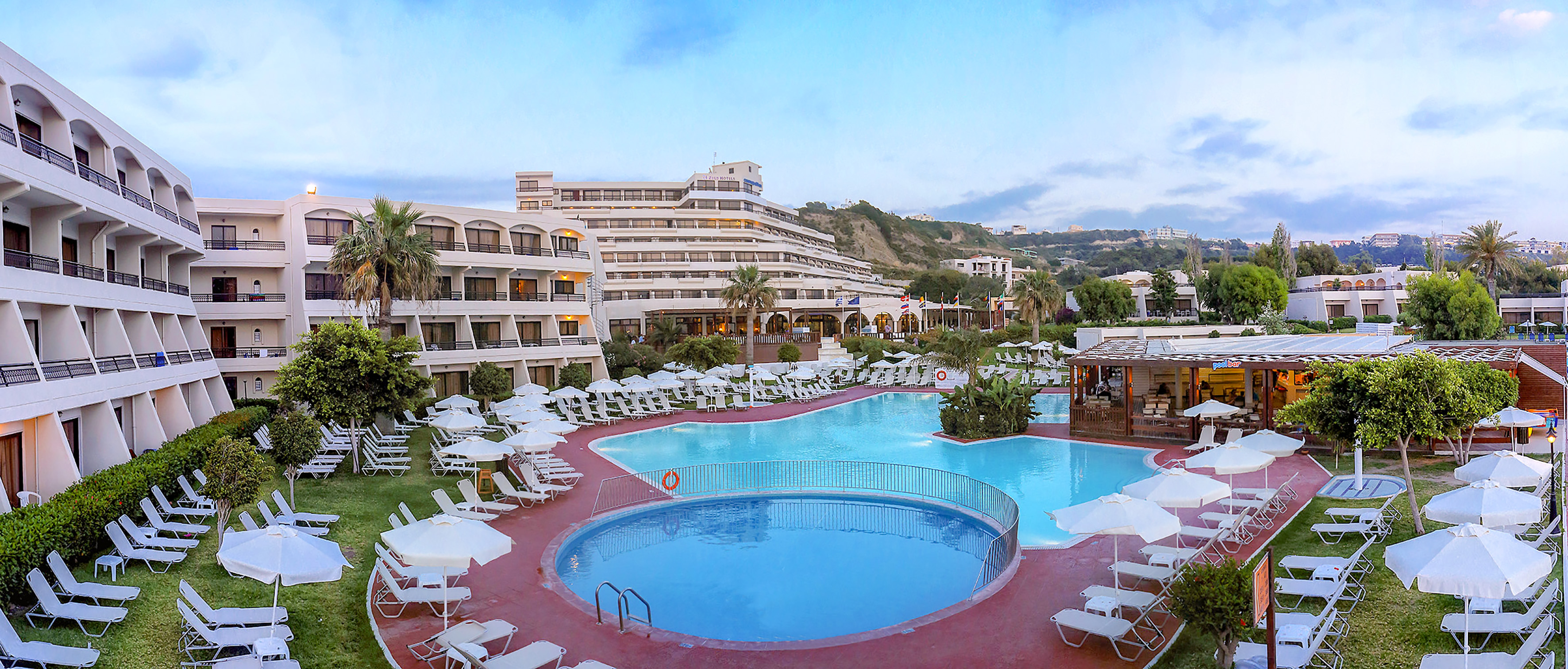 a pool with chairs and umbrellas in front of a hotel