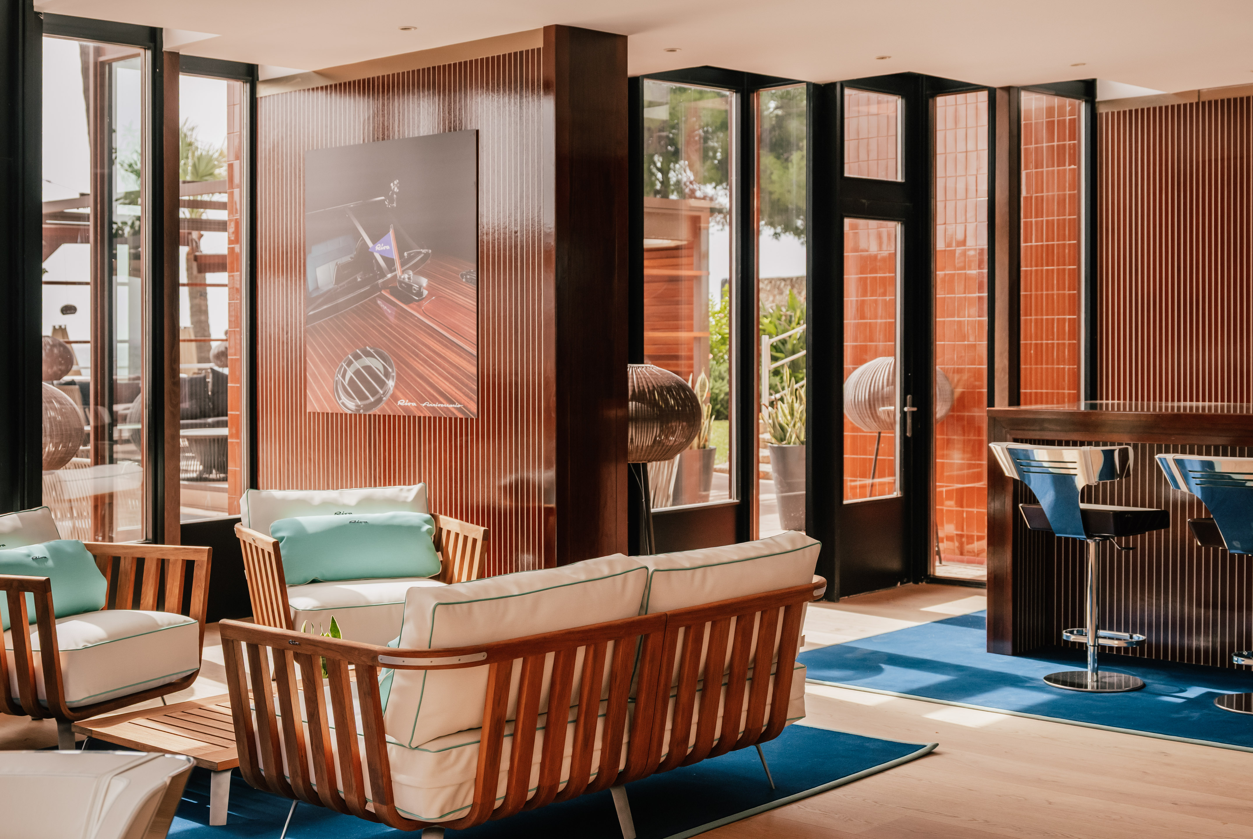 Modern lounge with wooden furniture, blue rug, and Riva boat artwork.